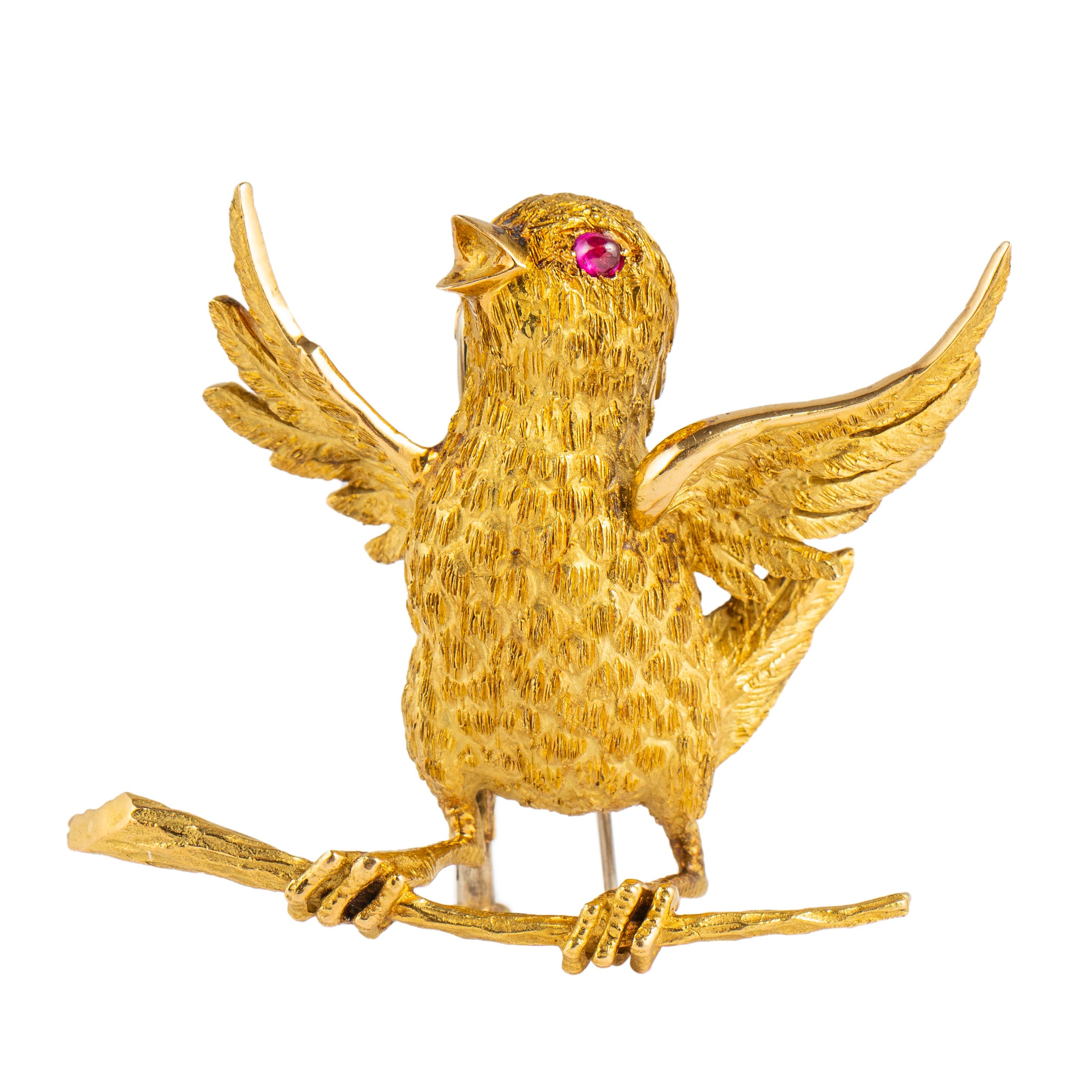 Delightful chirping chick in 18k gold with outstretched wings perched on a branch, the gold is beautifully textured to show its feathers and claws with a cabochon ruby as the eye, fitted with a double hinged clip and sliding sleeve, with London