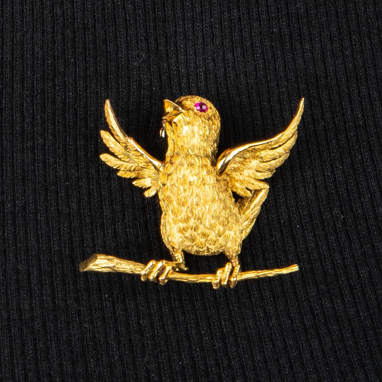 Delightful chirping chick in 18k gold with outstretched wings perched on a branch, the gold is beautifully textured to show its feathers and claws with a cabochon ruby as the eye, fitted with a double hinged clip and sliding sleeve, with London