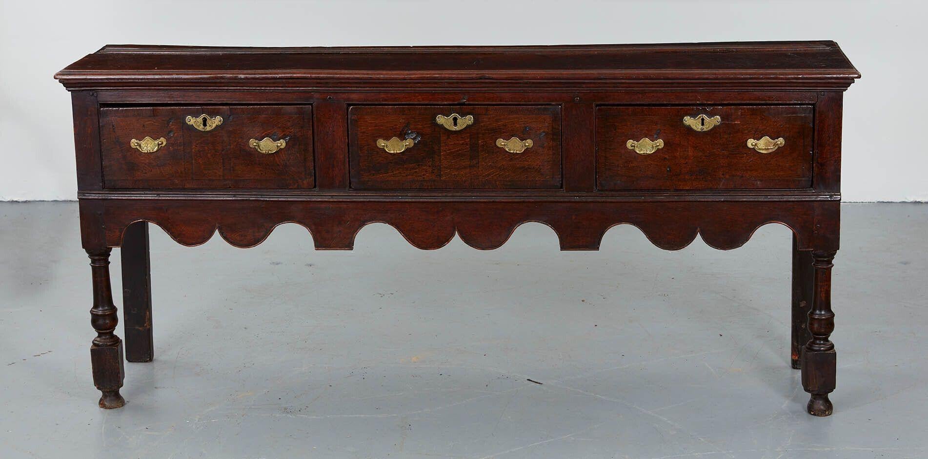 An 18th century dresser base in oak with an imposing stance and excellent color. Three drawers each with two handles and an escutcheon over a scalloped apron, standing on turned and blocked front legs.