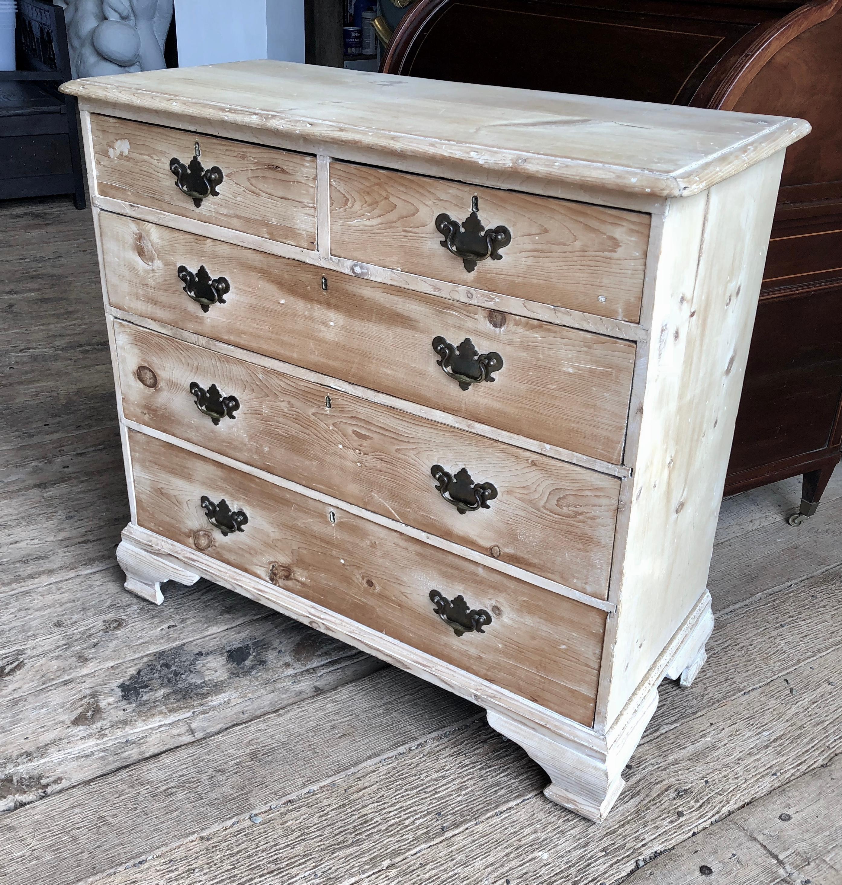 A late 18th century English chest of drawers in stripped and bleached pine, with two short drawers over three full drawers with ogee bracket feet and bat-wing brass pulls.