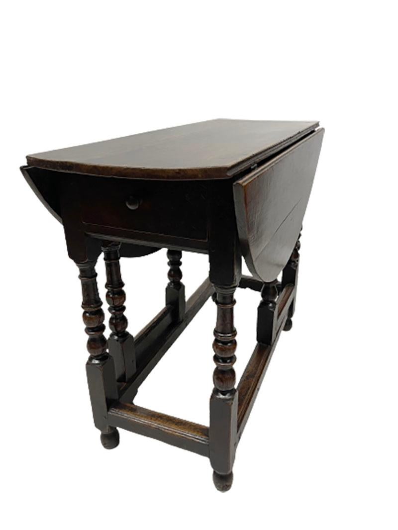 English 18th century gateleg table. 

An Oak drop-leaf gateleg table with folding sides, resting on turned column legs. On 1 side there is a drawer with a round wooden knob. The dimensions are 74 cm high, 104.5 cm wide. Deep with sides down is