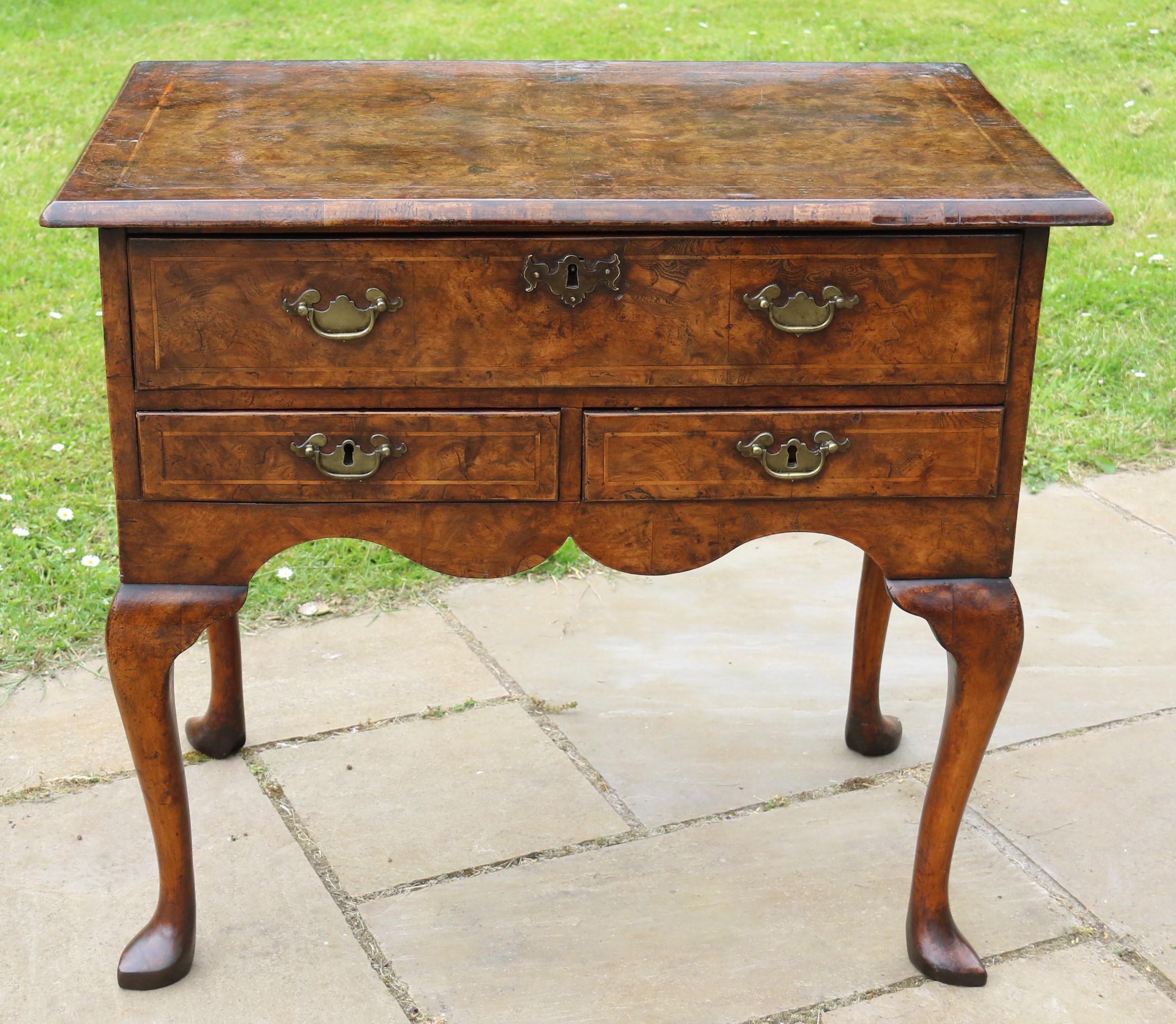 Esta rara y bella pieza de mobiliario inglés de Jorge II es un mueble bajo chapado en olmo con ricas figuras. Se alza sobre patas cabriolé con pies almohadillados puntiagudos. Tiene tres cajones, el superior de anchura completa y un par de cajones