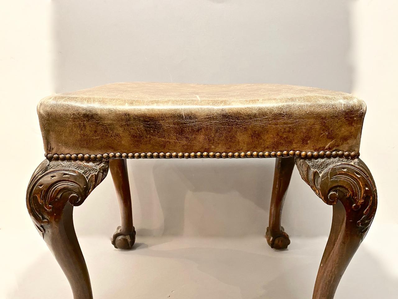 This is a great example of an 18th century English mahogany Chippendale or George III stool. The stool is upholstered in a caramel-toned vintage leather that shows just the right amount of patina and is further detailed in nail heads. The stool is