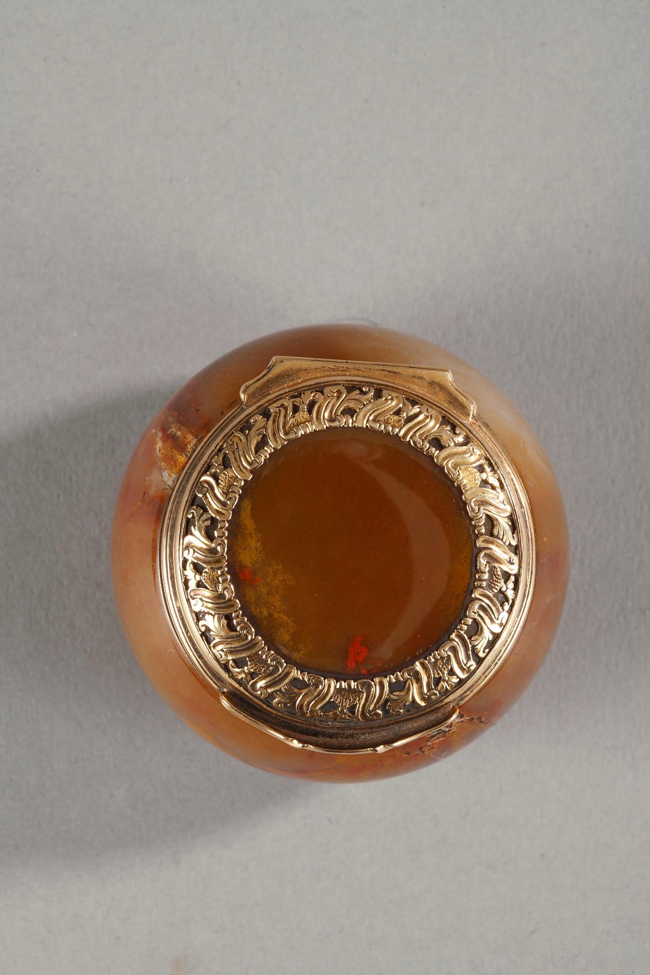 Agate box or snuff-box in of circular form with gently bombé sides, the gold mounted lid is chased with scrollwork.
Probably Georges II period.
Unmarked gold. Some usual wear, 18th century.
W: 1.94oz (55g).
Measures: L 1.57in. (4.5 cm) / l