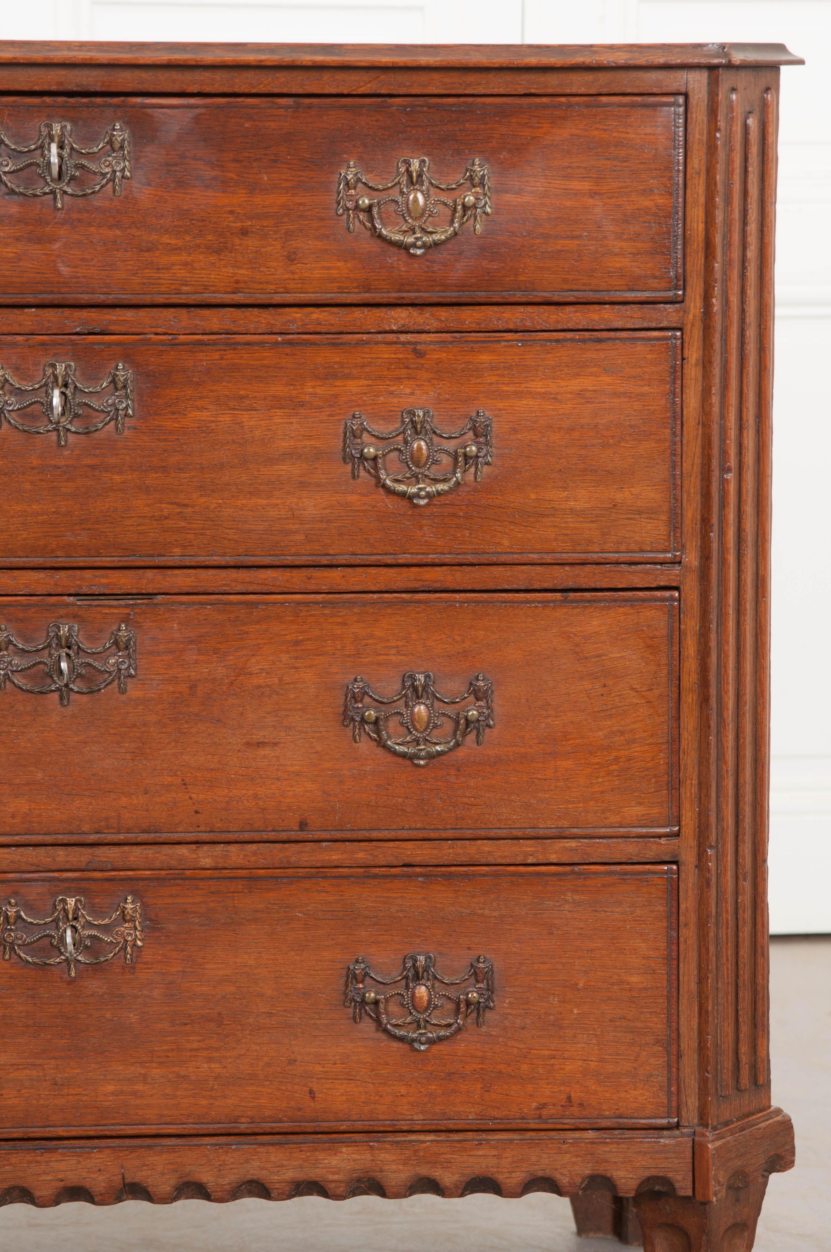 This Jacobean oak chest of drawers is from 1780's England, and features a conforming top over canted and reeded corners. It has four long drawers each with a different lock and beautifully detailed drawer pulls, over a charming scallop-carved apron