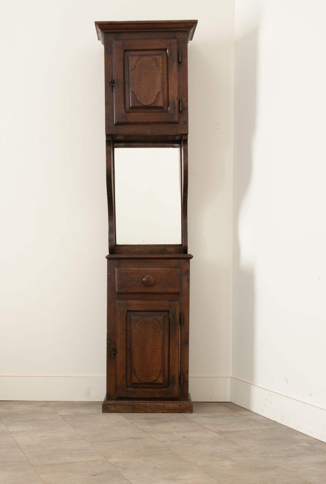 This unique storage unit was handcrafted in England during the 1780’s from solid oak. The upper cabinet door has provincial carvings and conceals a space with a single shelf. A newly installed rectangular mirror is flanked by curved forms,