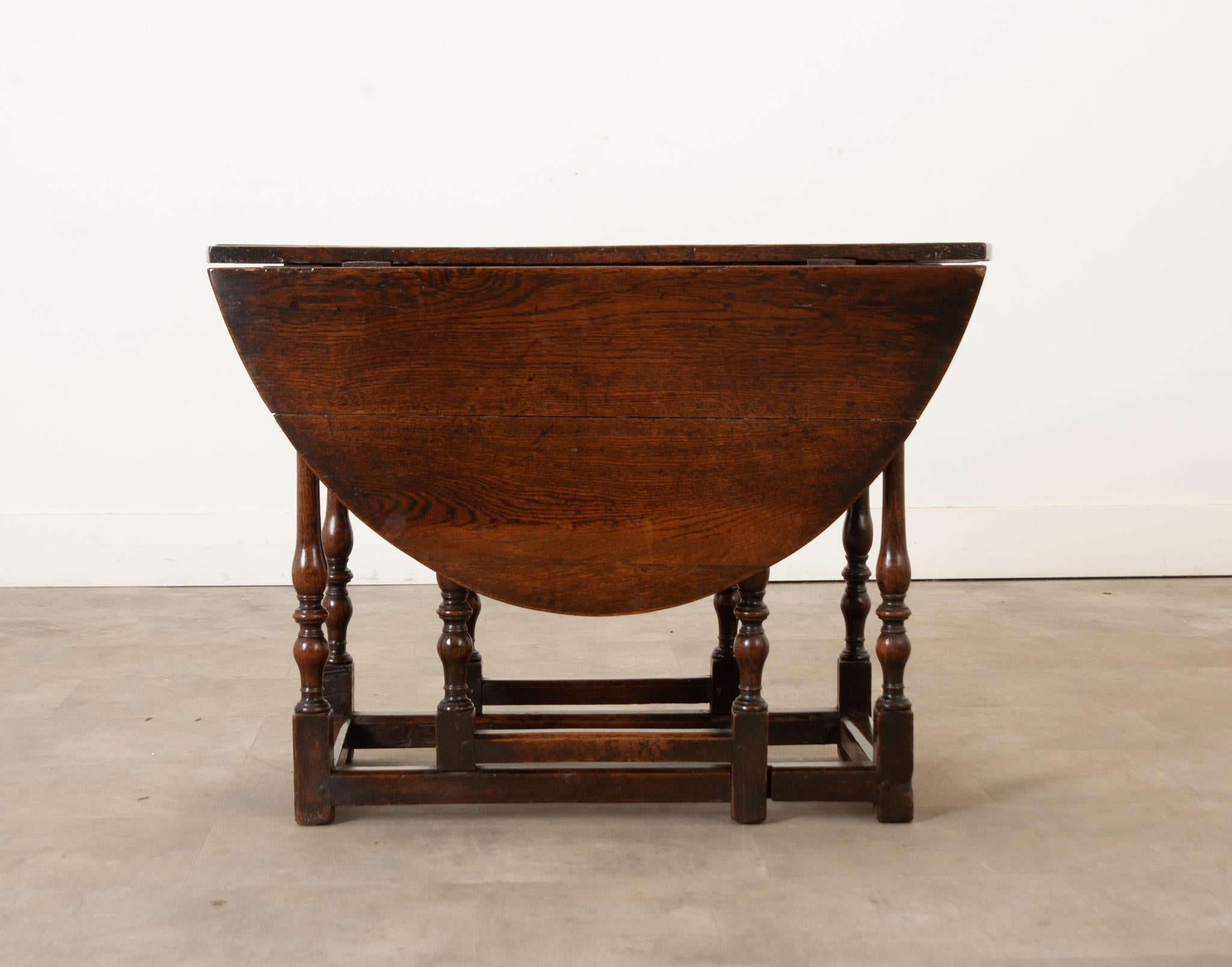 English 18th Century solid oak gateleg table. This table boosts charm and patina only possible with its age and construction. The table is held together with peg joinery and hand cut steel hinges. The oval drop leaf table top is connected to turned