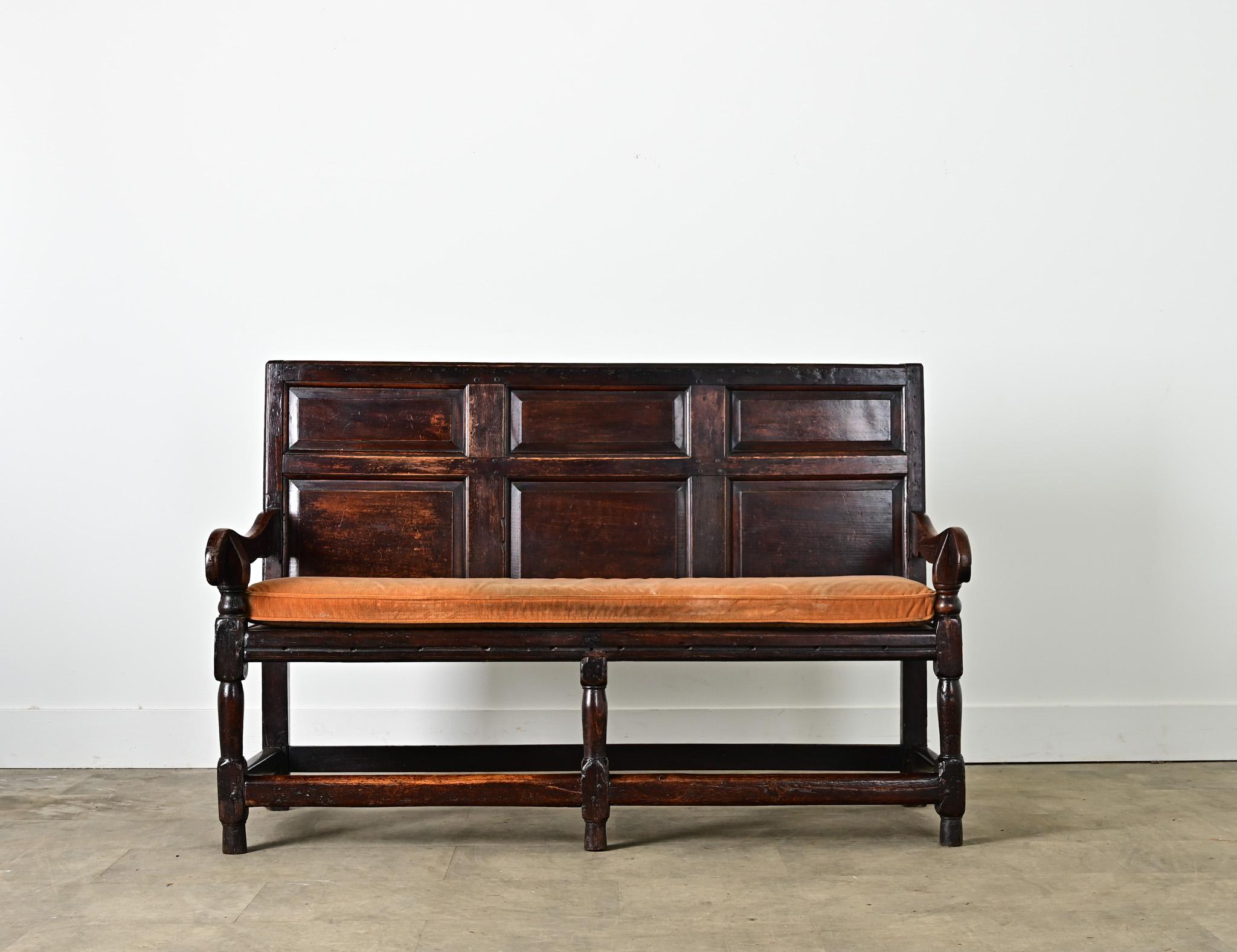 A circa 1780 English settle or hall bench in solid oak with paneled back and removable bench cushion. After nearly three centuries the wood appears ebonized with dark patina that enhances the sharp angles of the recesses in the paneling. The