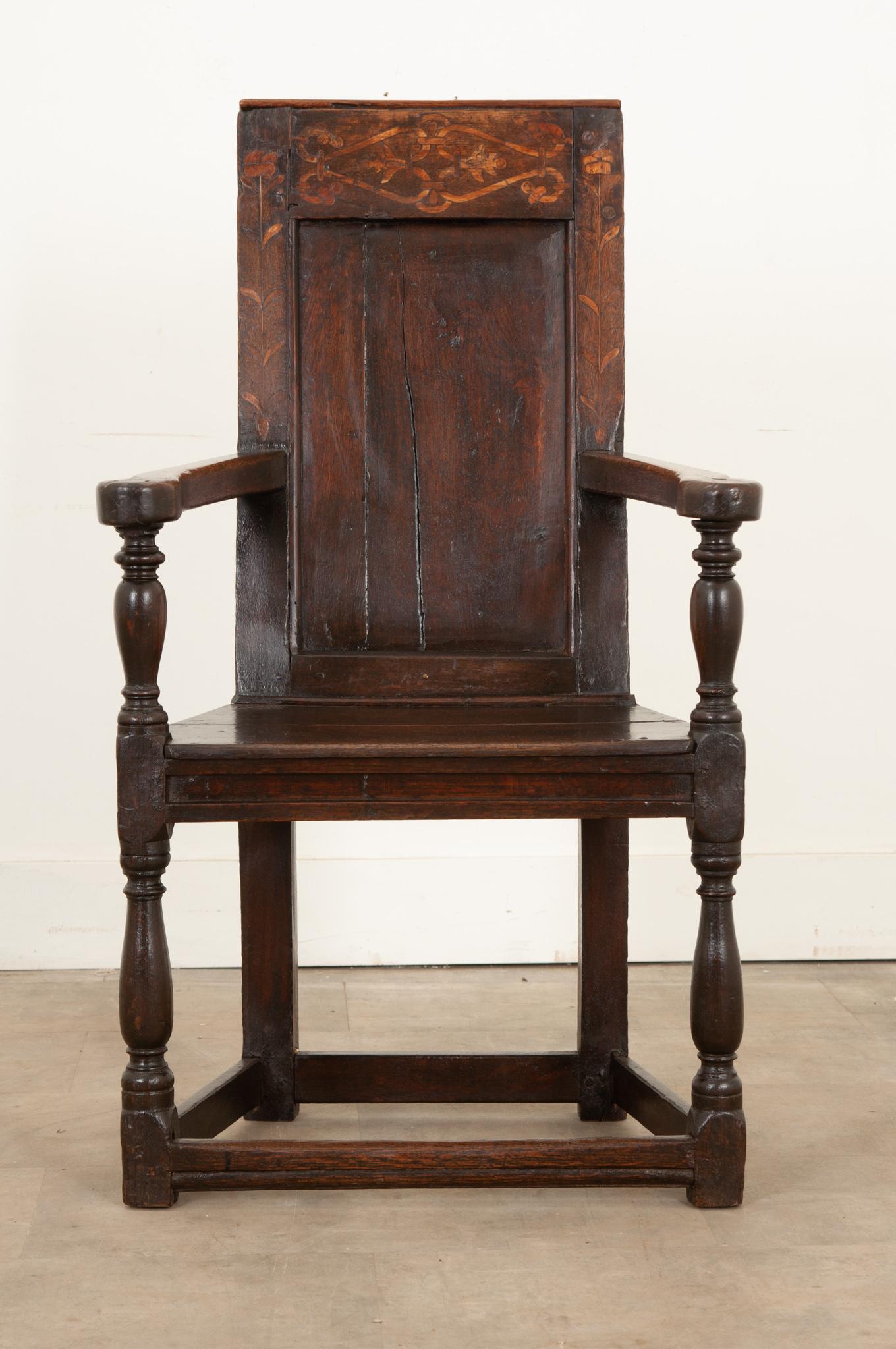 A rare and impressive 18th century English wainscot armchair hand-carved from solid oak. A highly decorative and original piece hand-crafted circa 1750 with inlaid floral and foliate motifs on a molded and trimmed back panel. Featuring smooth broad