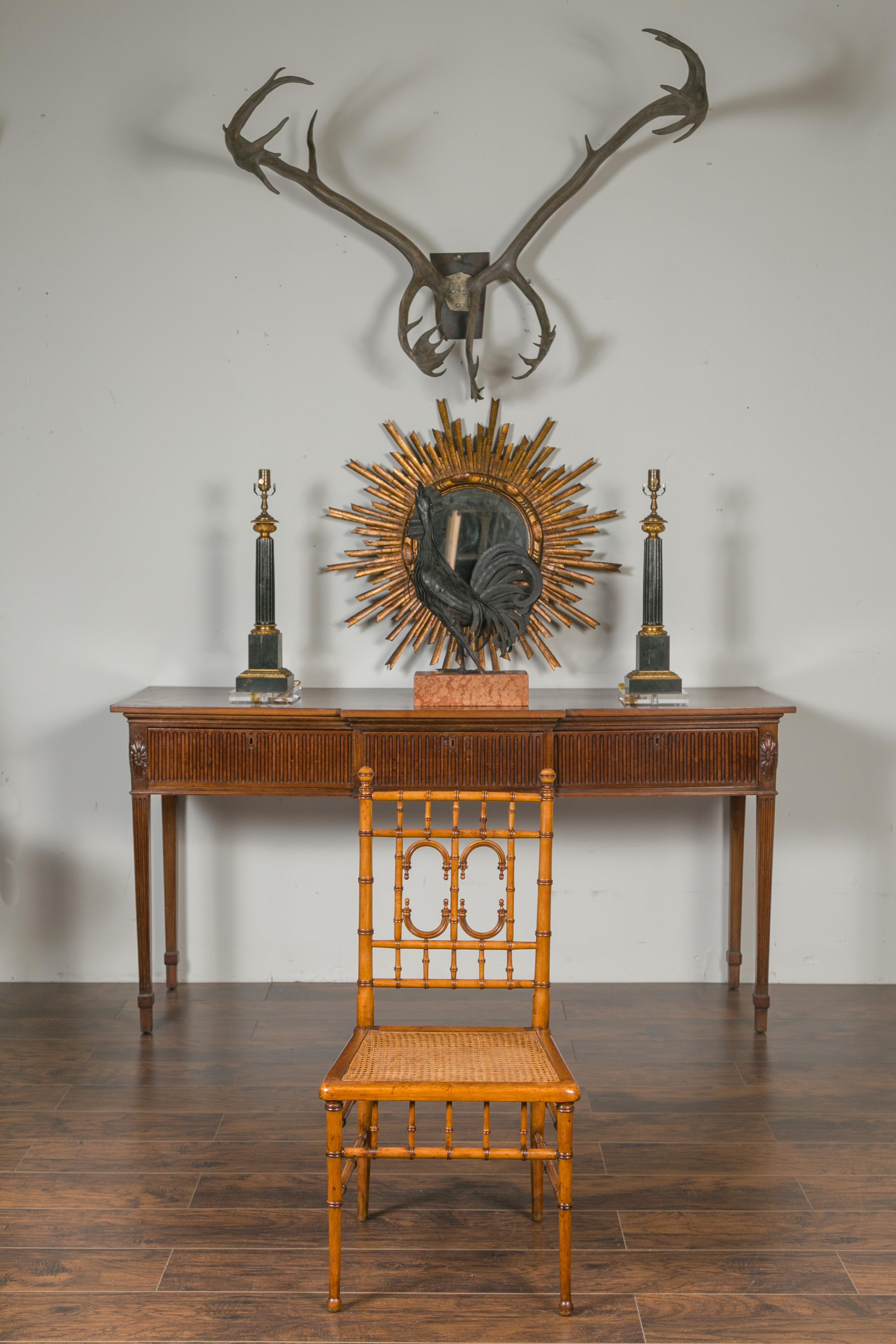 An English bamboo side chair from the early 20th century, with cane seat, arched motifs and ball feet. Crafted in England during the Turn of the Century, this bamboo chair features a slightly slanted back adorned with arched motifs, flowing