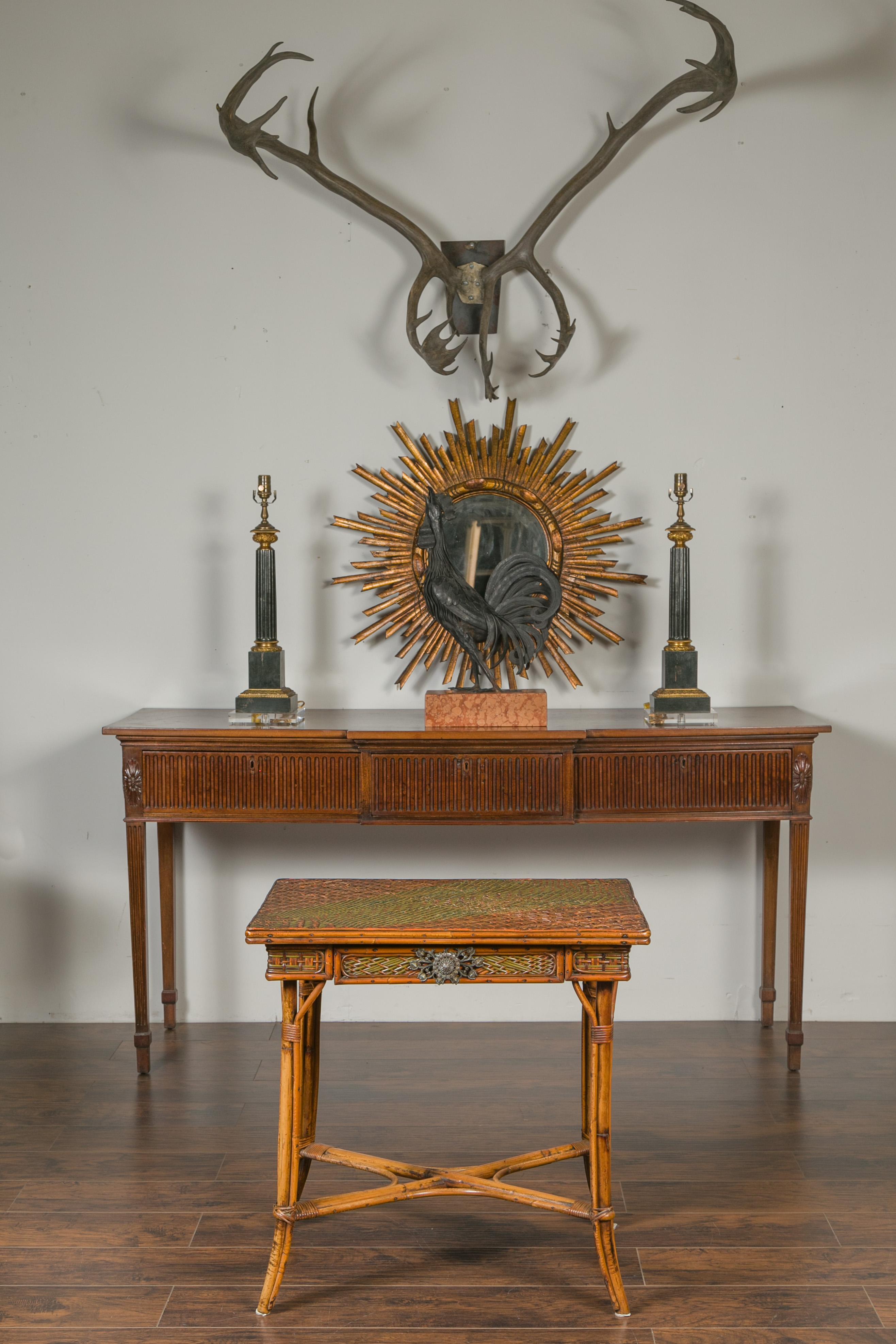 An English bamboo side table from the early 20th century, with rattan top and ornate hardware. Created in England at the turn of the century, this bamboo side table features a two-toned rattan top sitting above a single drawer fitted with exquisite