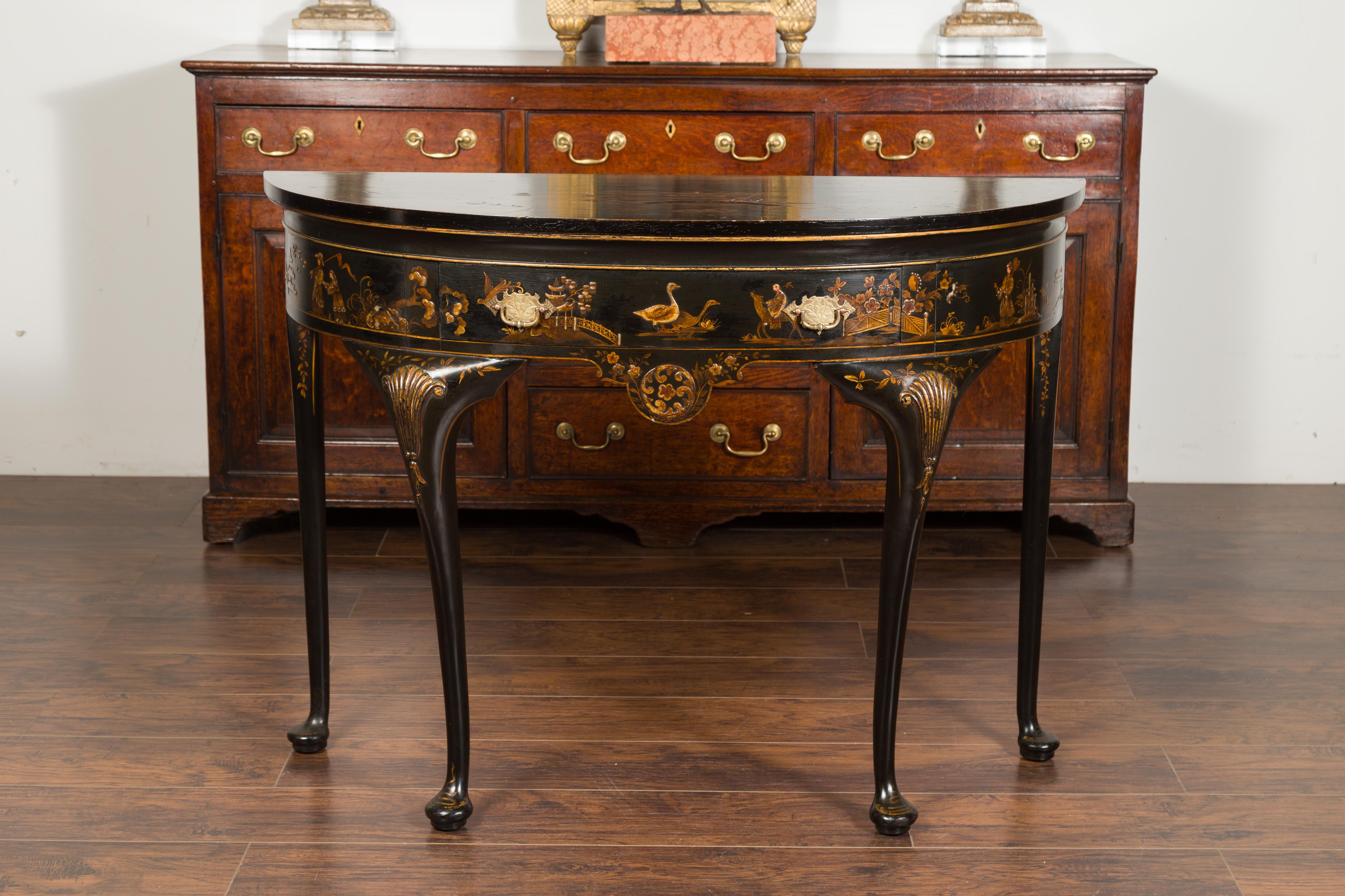 An English black and gold demilune table from the early 20th century, with chinoiserie decor and single drawer. Created in England during the early years of the 20th century, this demilune features a semi-circular top sitting above a single drawer
