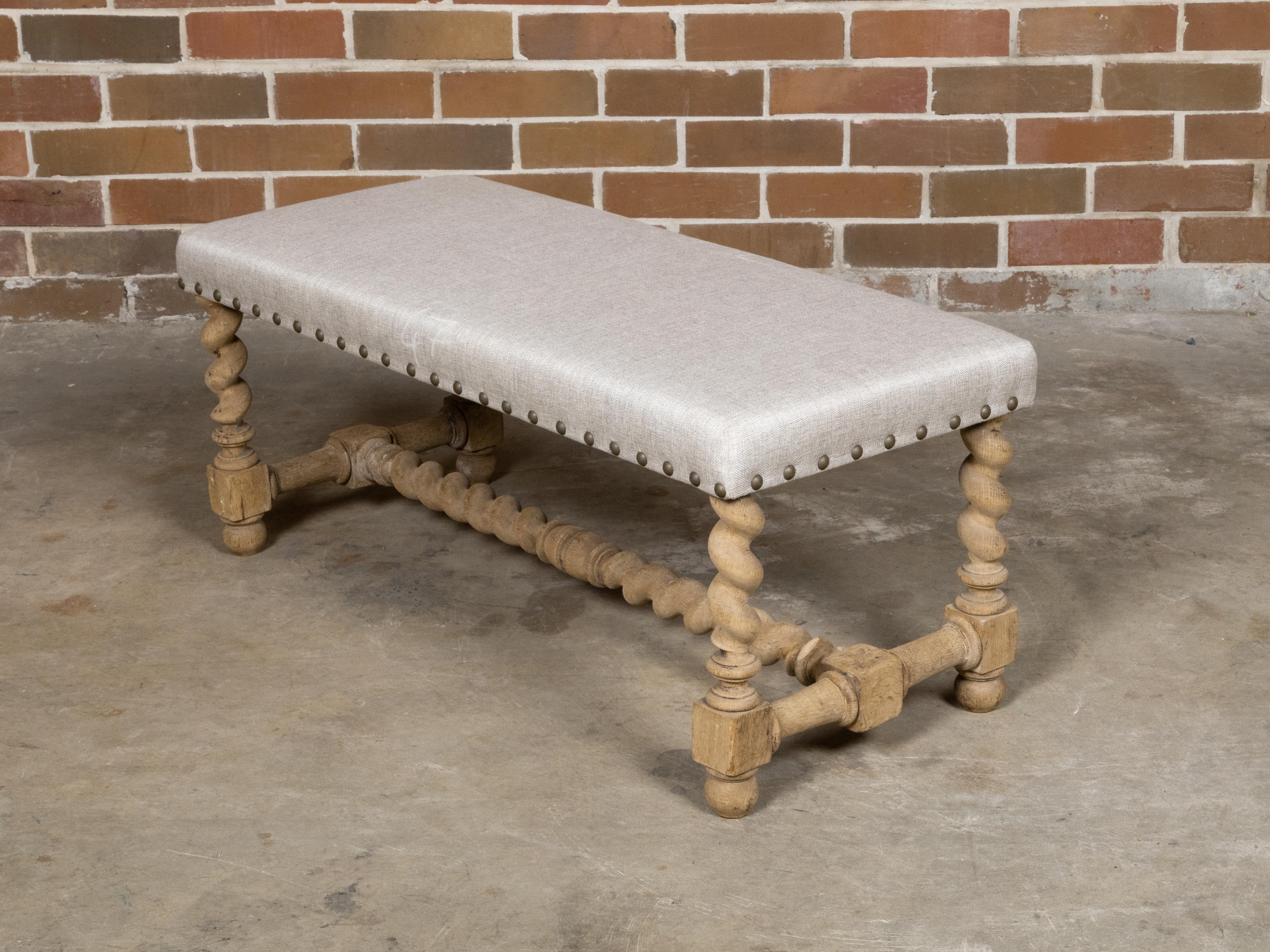 An English bleached wood bench from circa 1900 with barley twist base and custom linen upholstery. This exquisite English bleached wood bench, hailing from circa 1900, captures the timeless elegance of the era with its unique barley twist base and