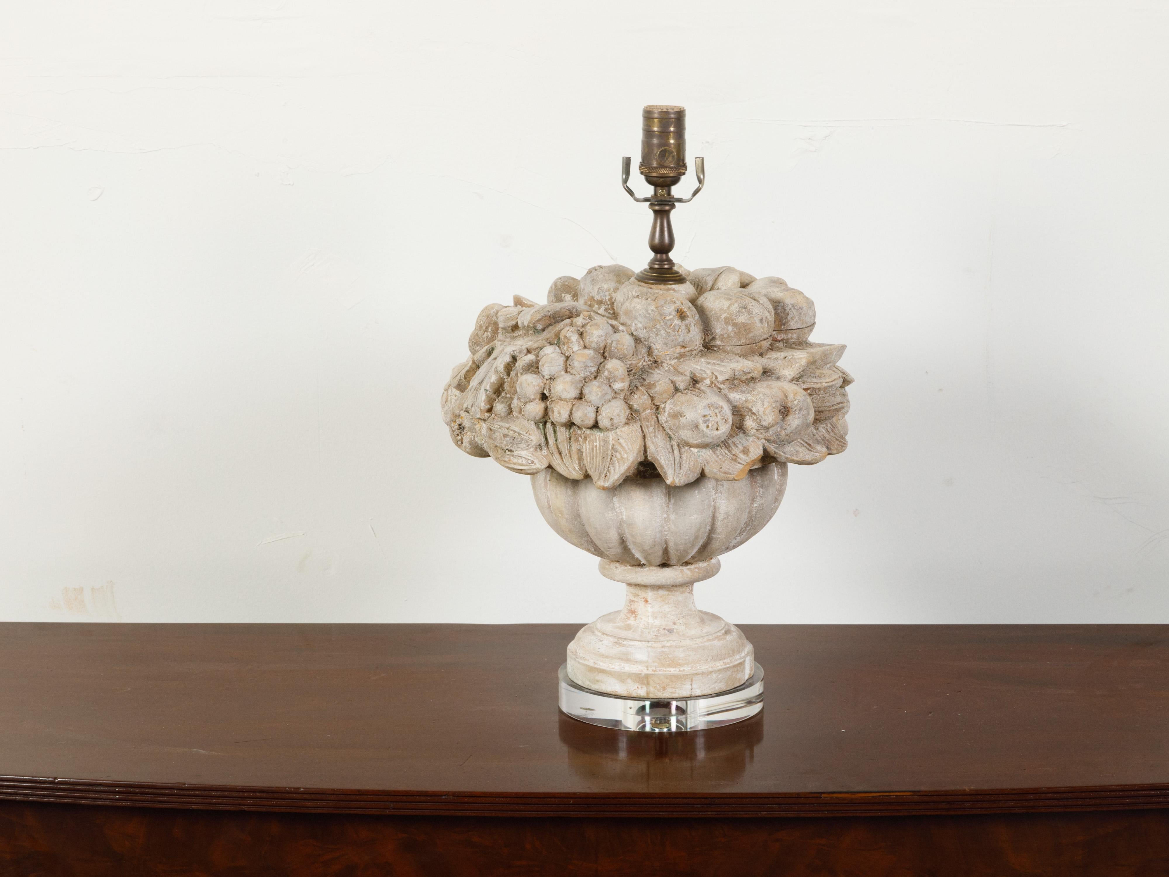 An English carved wooden fragment table lamp from the early 20th century, depicting a vessel overflowing with fruits and mounted on lucite base. Created in England during the first decade of the 20th century, this sculpture charms us with its
