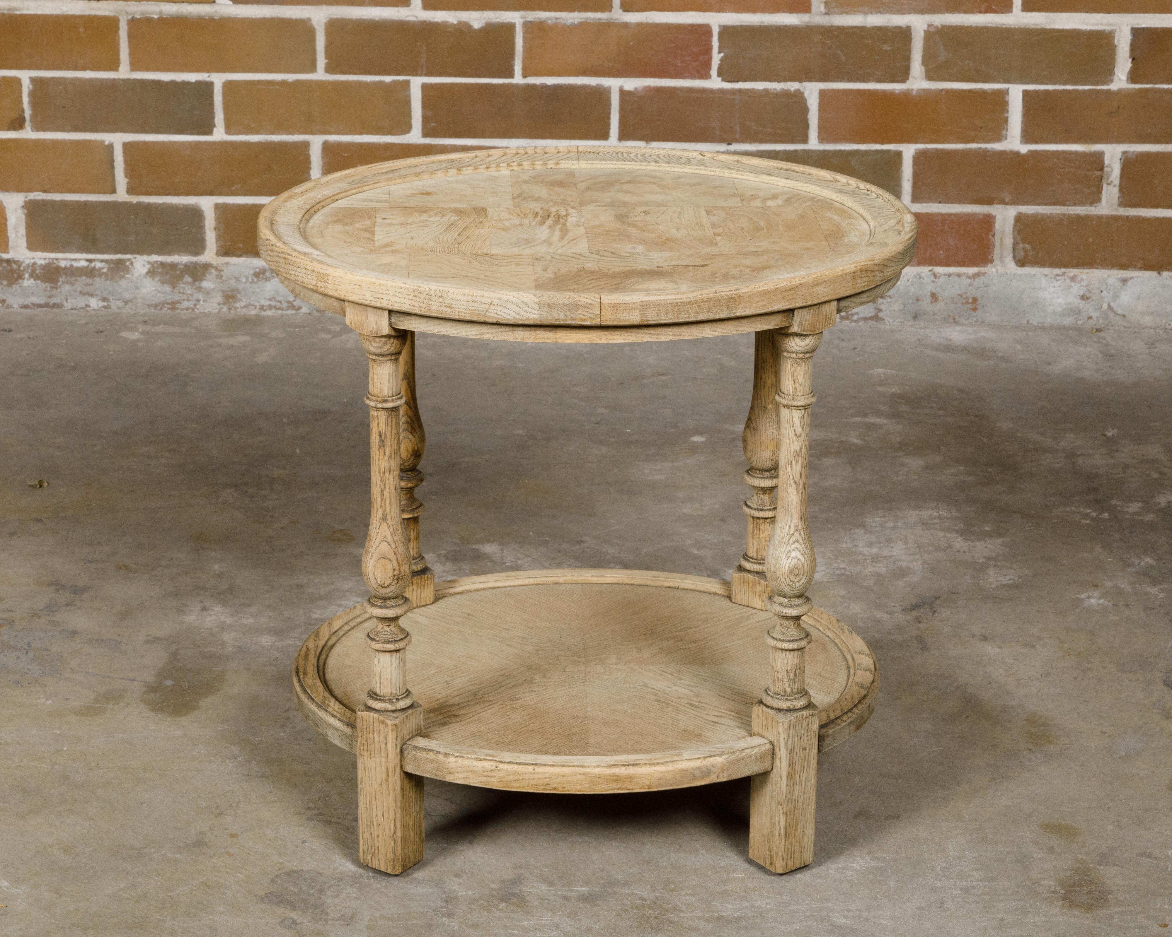An English bleached elmwood veneered oval side table from circa 1900 with two tiers, turned baluster legs and rectangular block joints. This English side table, gracefully crafted from bleached elmwood veneer, showcases a timeless oval design
