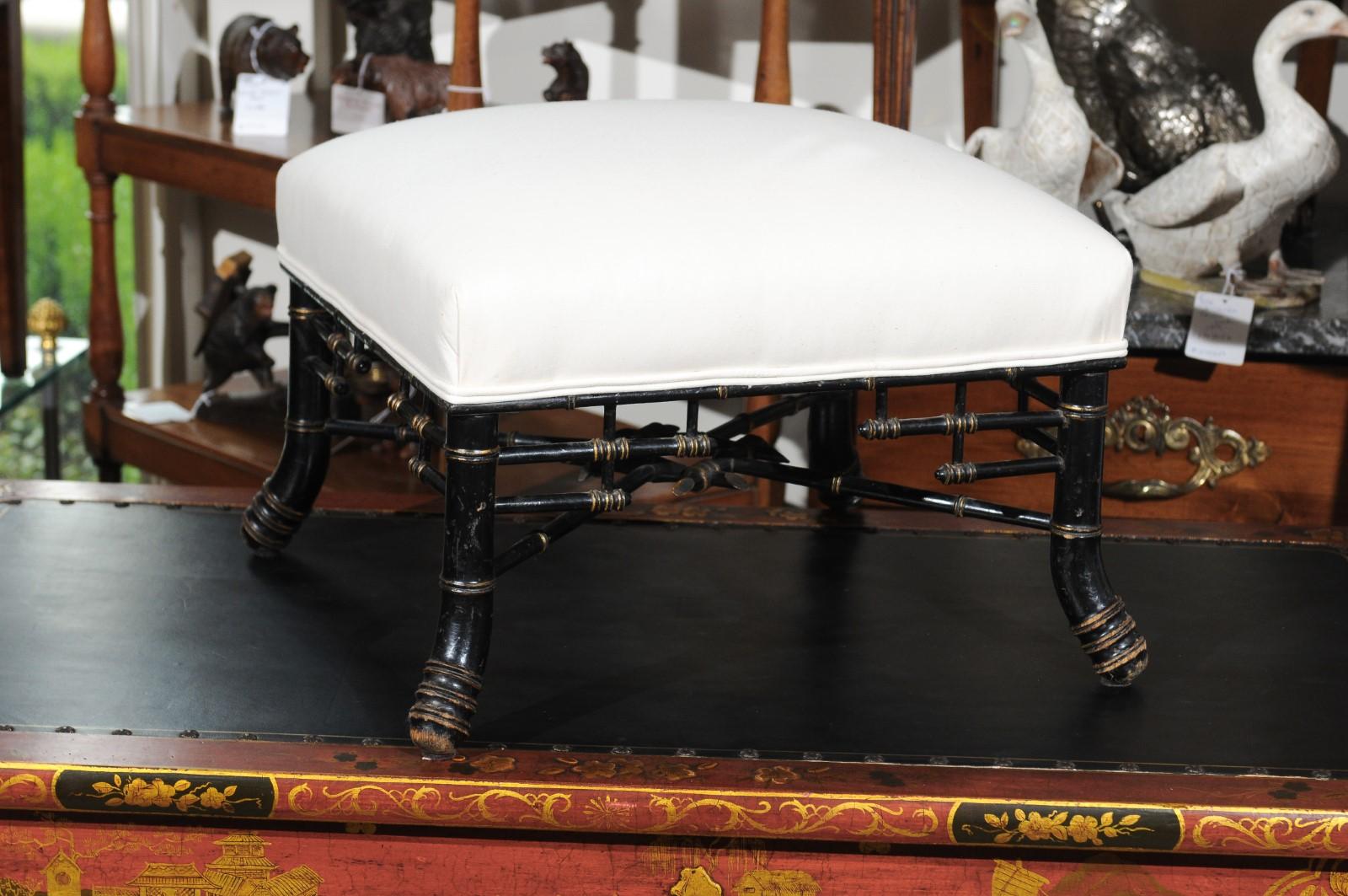 An English Chinese Chippendale style ebonized wood footstool from the early 20th century, with newly upholstered seat. Born in England during the reign of King Edward VII, this stylish Chinese Chippendale style stool features a square top, covered