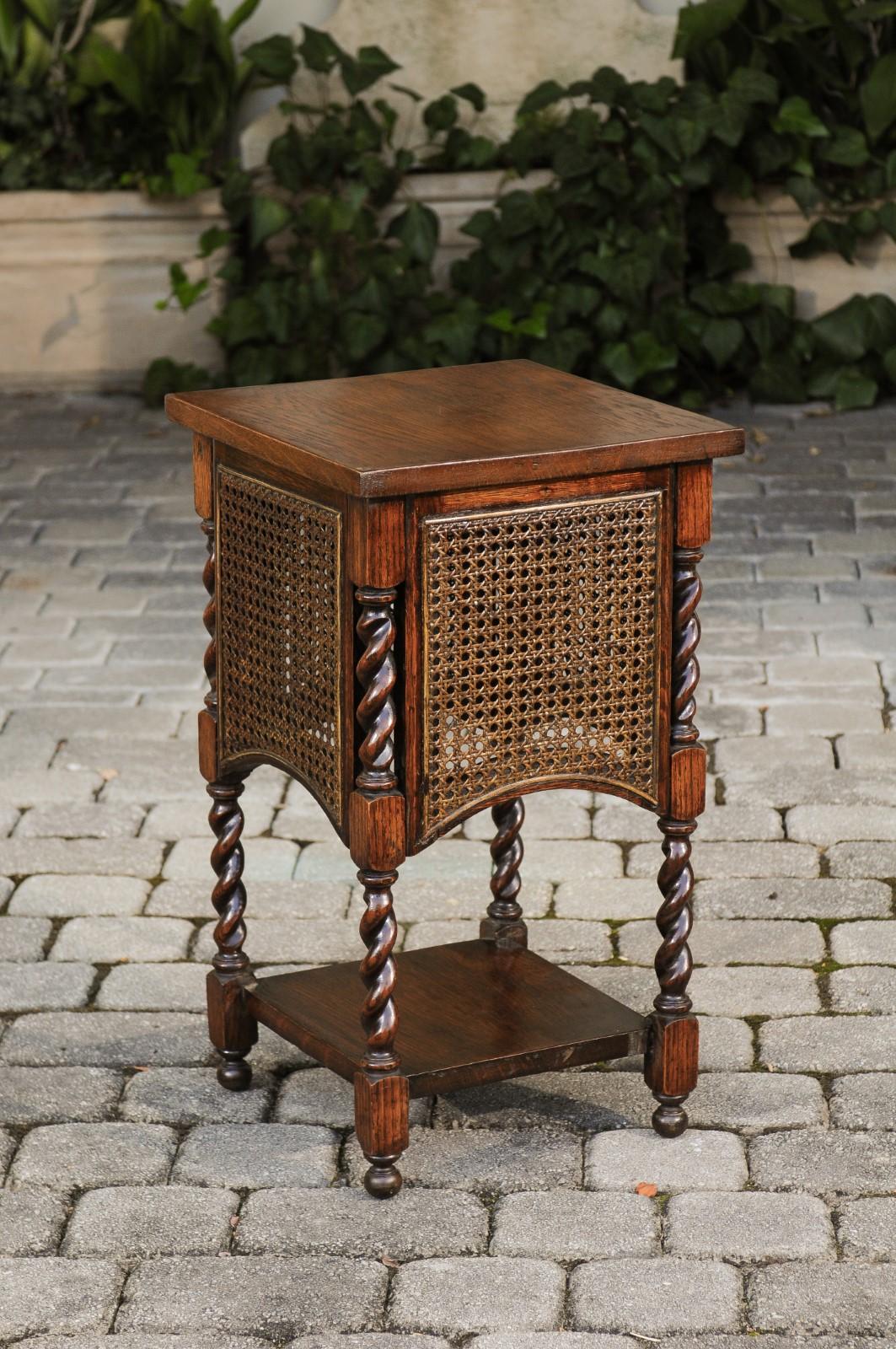 An English oak side table from the early 20th century, with barley twist accents and cane sides. Born in England at the turn of the century, this exquisite side table features a square top sitting above four cane panels arched in their bottom part