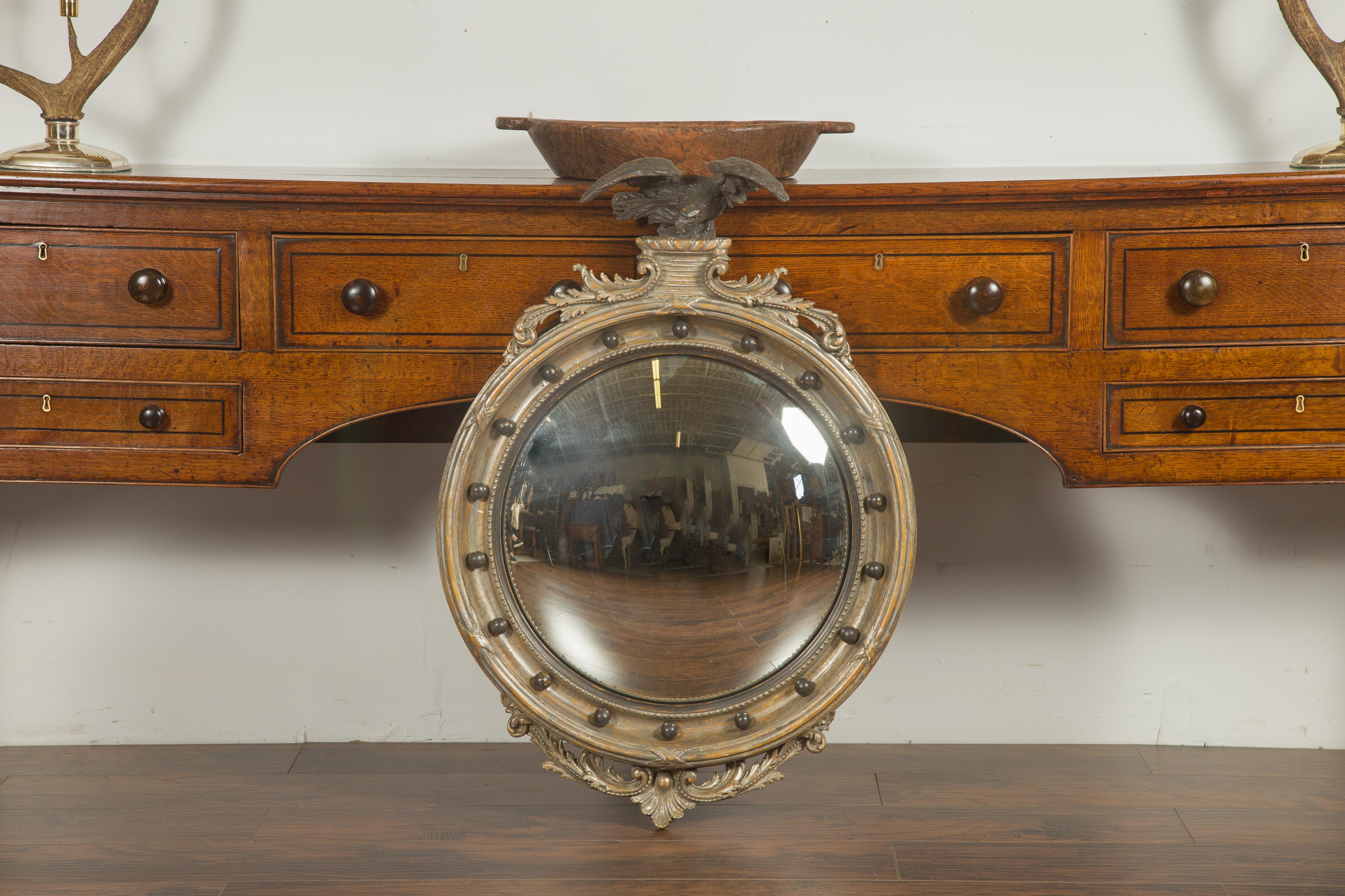 An English silver leaf convex girandole bullseye mirror from the early 20th century, with carved eagle motif and volutes. Created in England during the early years of the 20th century, this silver leaf girandole mirror attracts our attention with