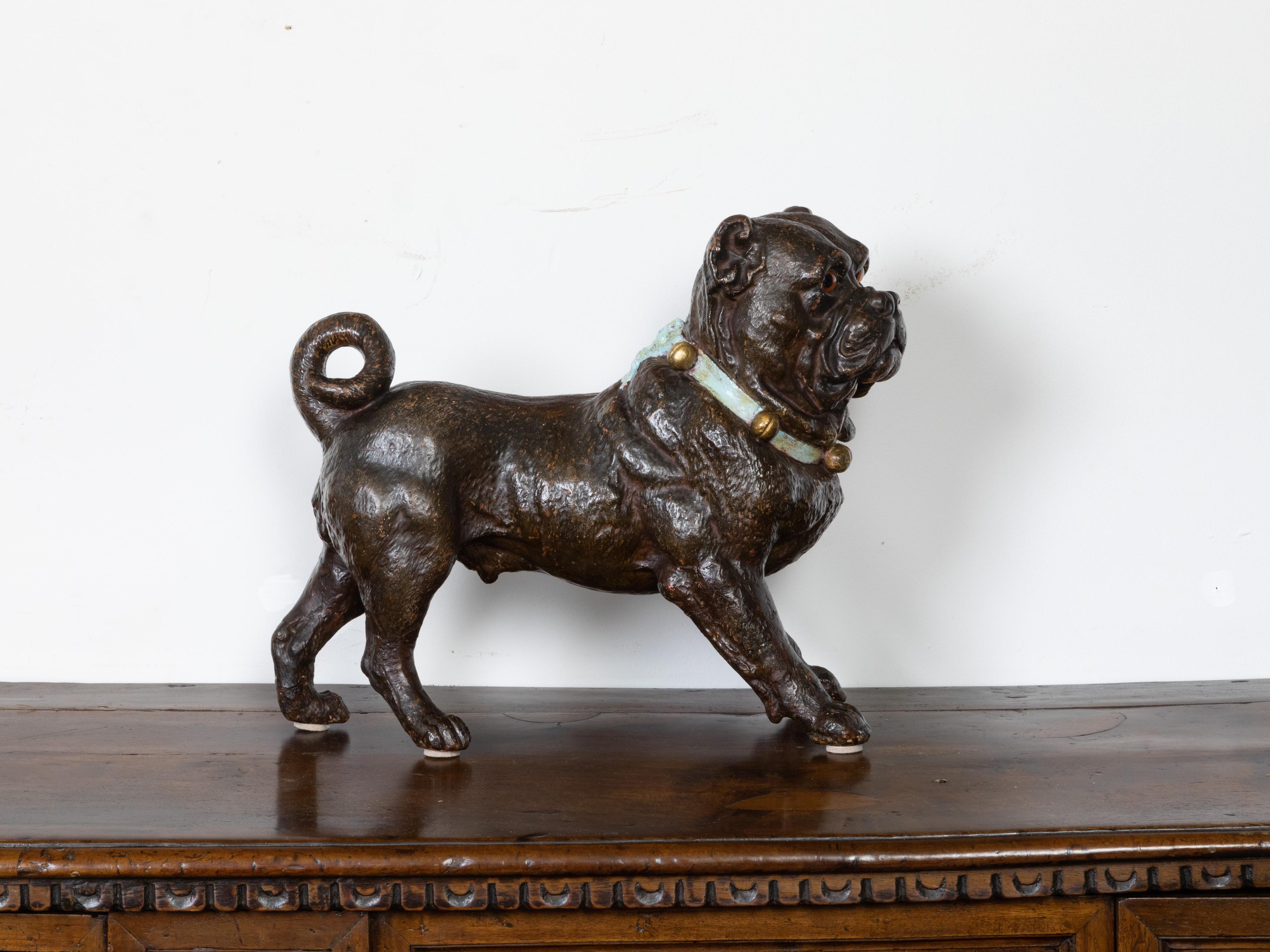 An English terracotta standing dog sculpture from the early 20th century, with glass eyes, green collar and bells. Created in England during the early years of the 20th century, this terracotta dog sculpture features a pug standing firmly on his