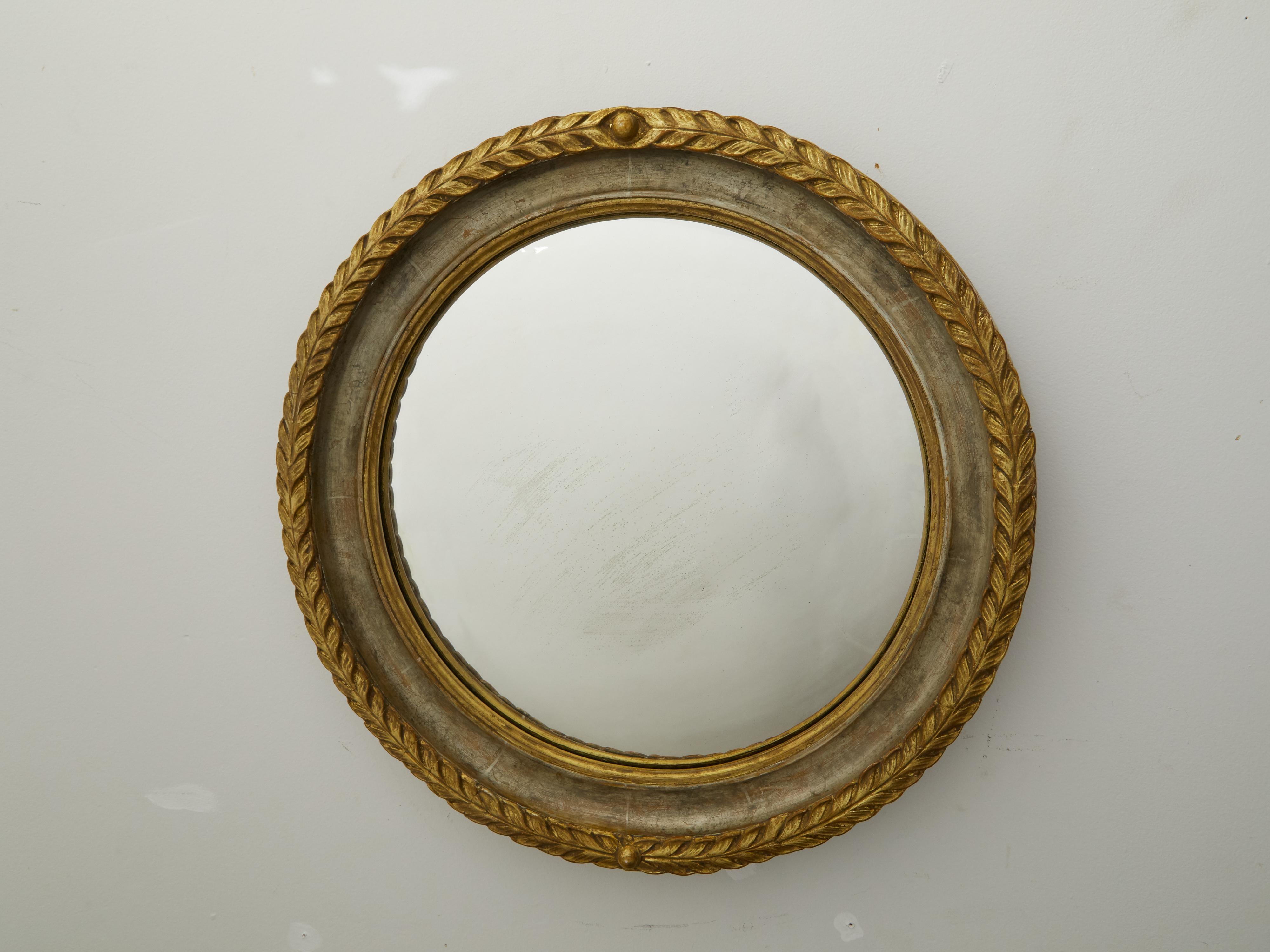 An English carved wooden circular mirror from the early 20th century, with foliage motifs and gilt accents. Created in England during the second quarter of the 20th century, this mirror features a round gilt frame adorned with foliage motifs on the