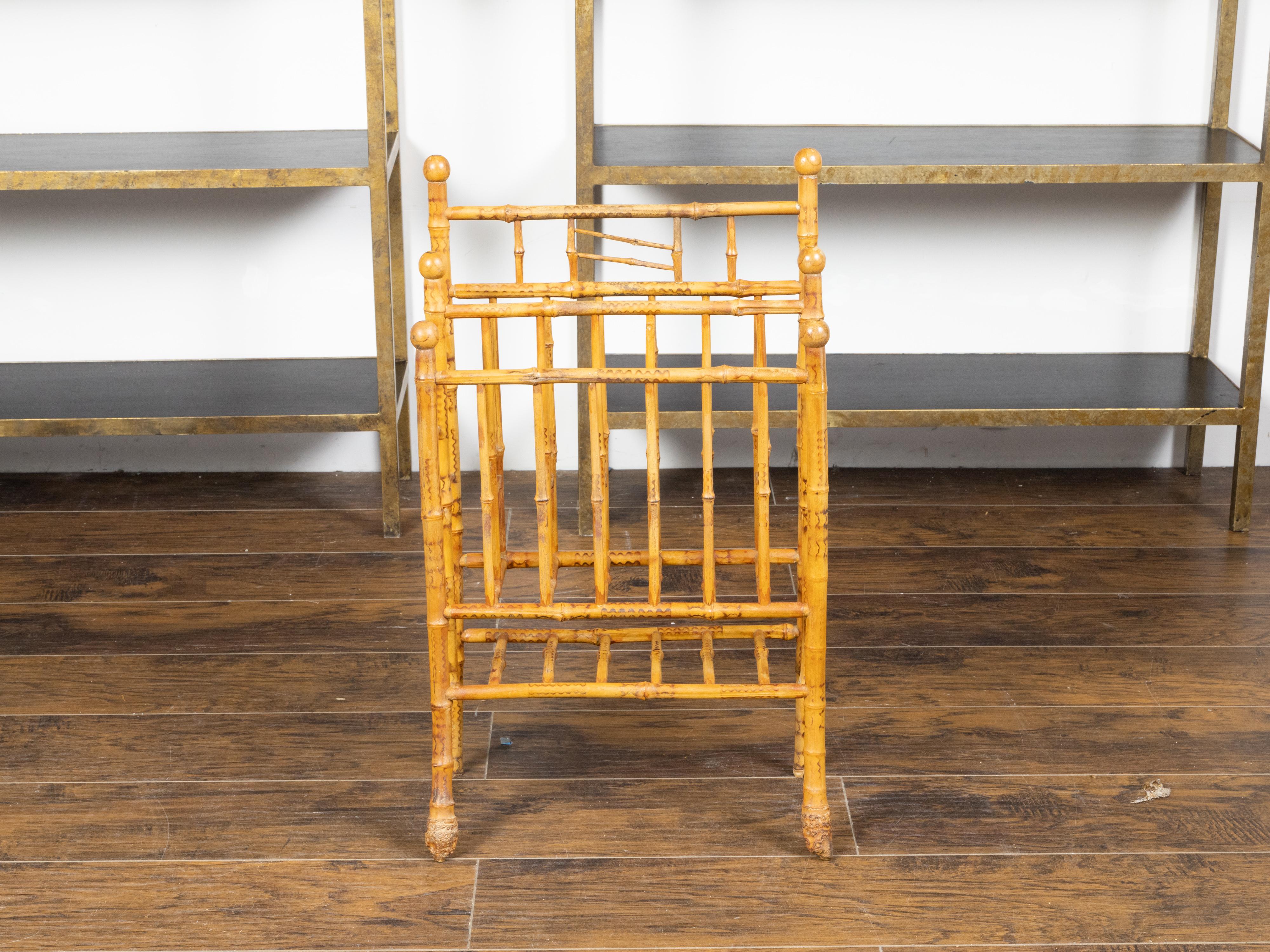 An English bamboo magazine rack from the early 20th century, with root feet, wavy motifs and petite finials. Created in England during the first quarter of the 20th century, this elegant magazine rack features a bamboo structure boasting a warm