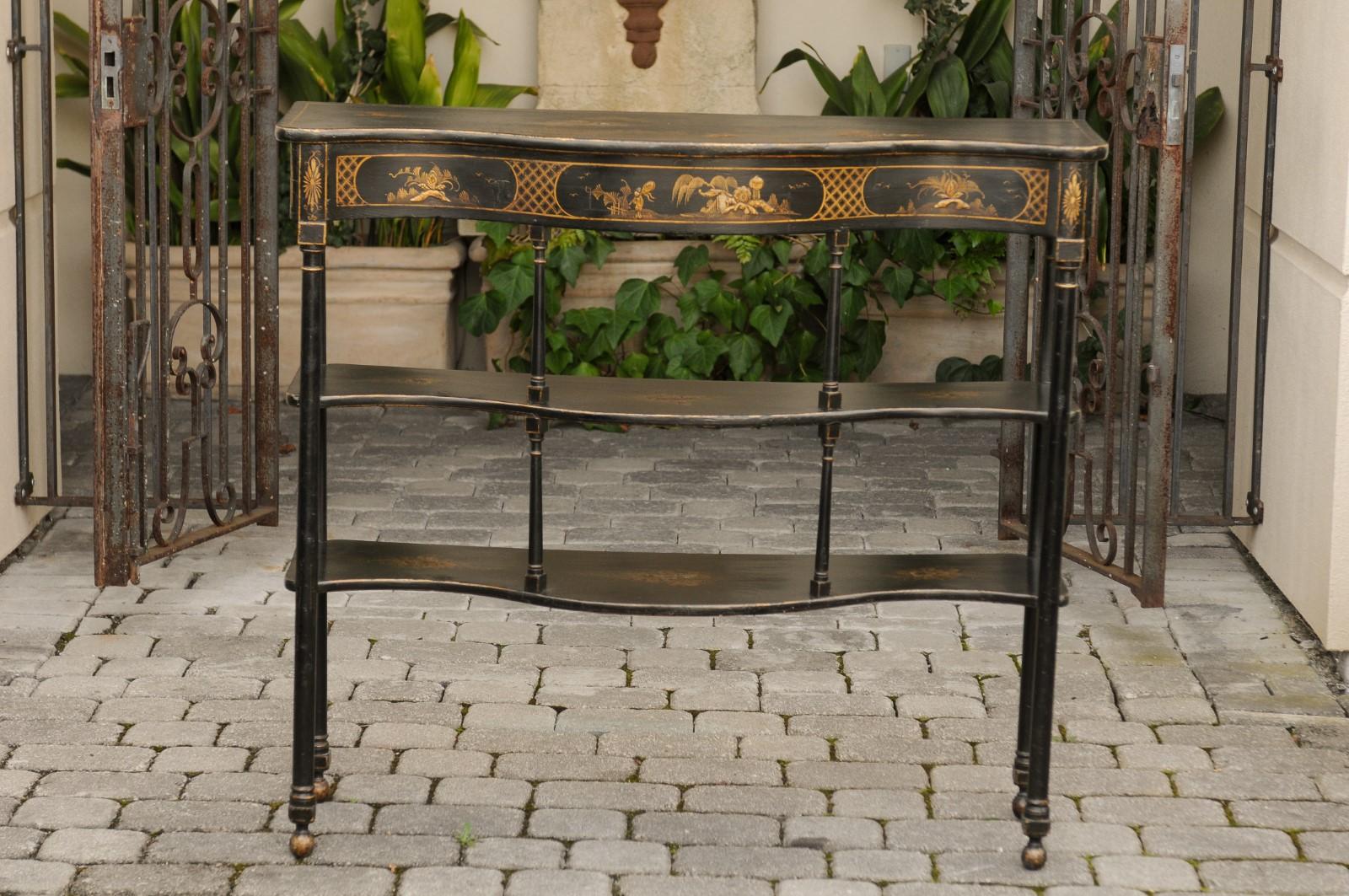 An English chinoiserie tiered console table from the first quarter of the 20th century, with serpentine front and hand-painted scenes on black background. Born during the Roaring 1920s, this exquisite English console table features a serpentine top,