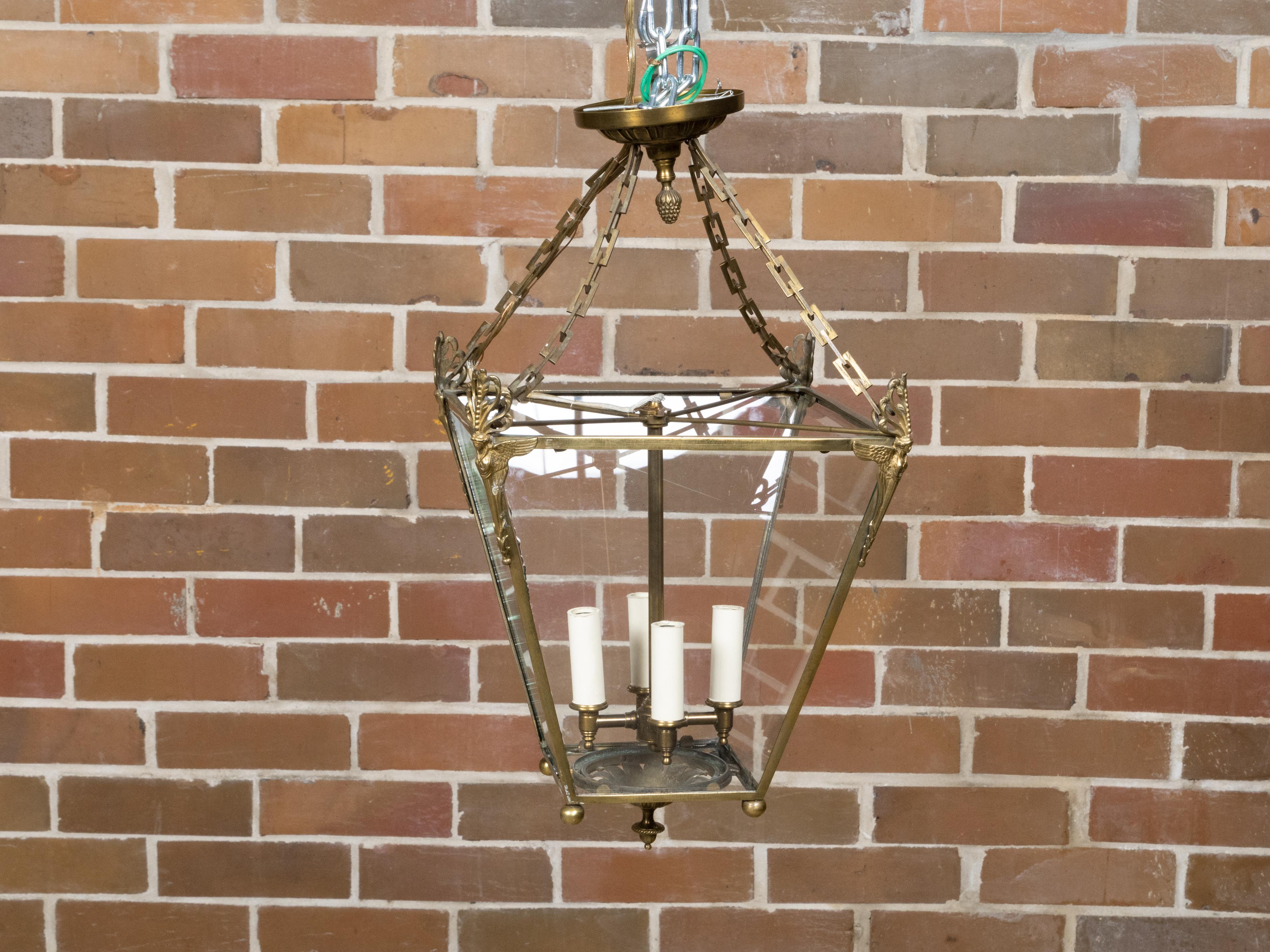 An English brass lantern from circa 1920 with four lights, angel motifs and glass panels. Created in England circa 1920, this exquisite brass lantern exudes a blend of elegance and subtlety, capturing the timeless charm of early 20th-century design.
