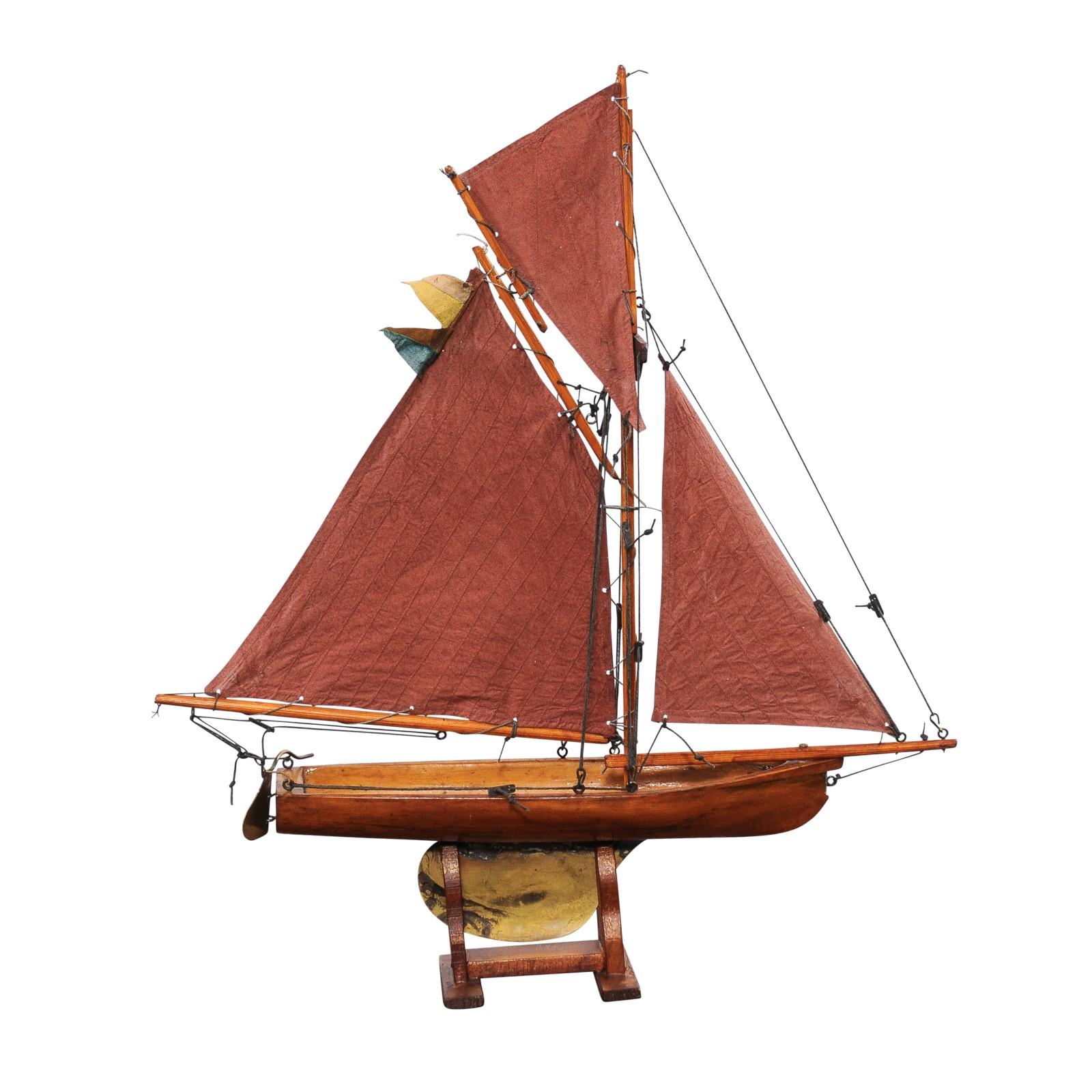 An English George V period Gaff Cutter pond yacht from circa 1920 with red sails on custom base. This elegant English George V period Gaff Cutter pond yacht, dating back to circa 1920, is a striking blend of nautical history and artistic