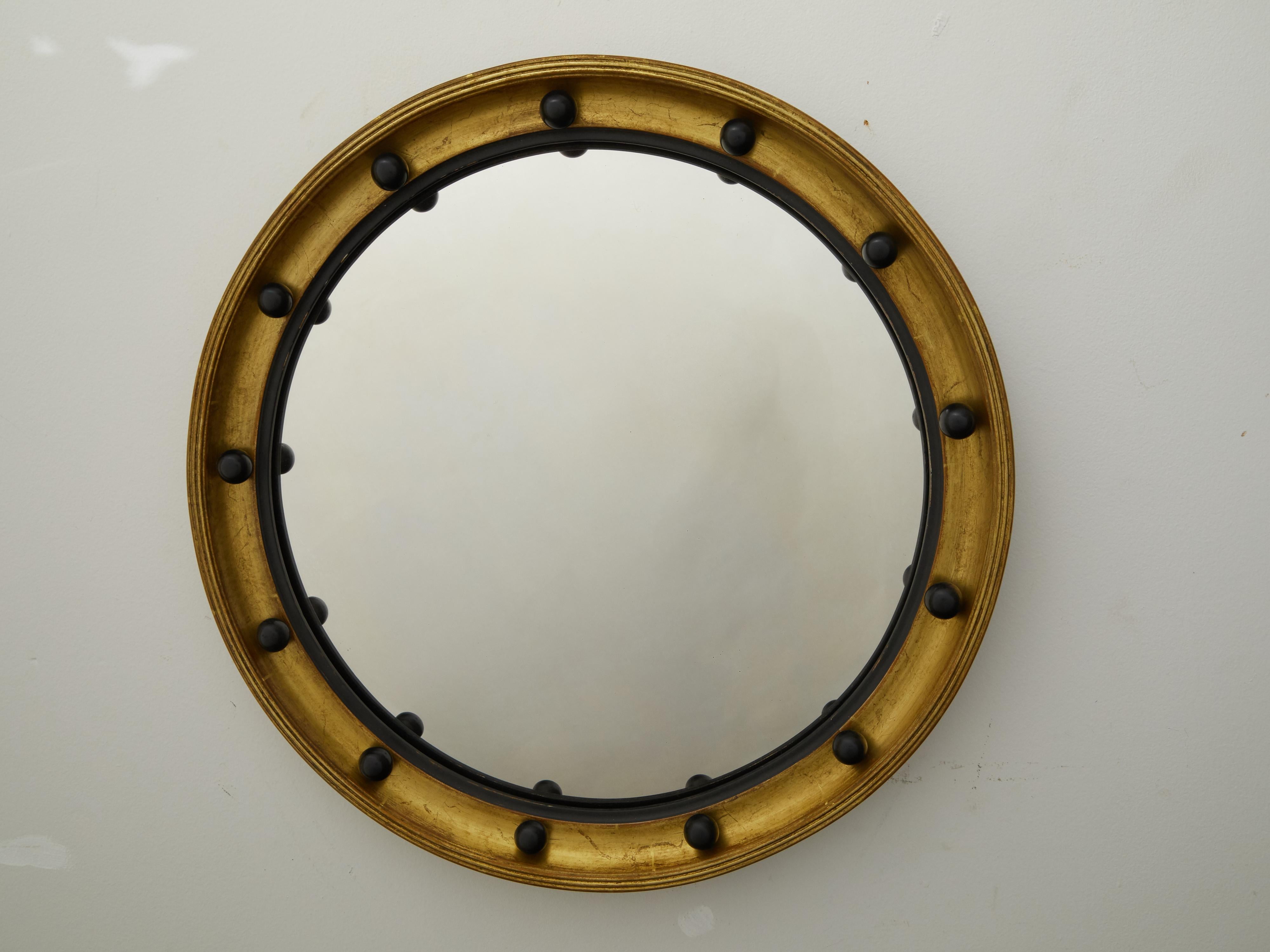 An English giltwood convex bullseye mirror from the early 20th century with dark spheres and inner molding. Created in England during the first quarter of the 20th century, this giltwood girandole mirror features a circular frame accented with