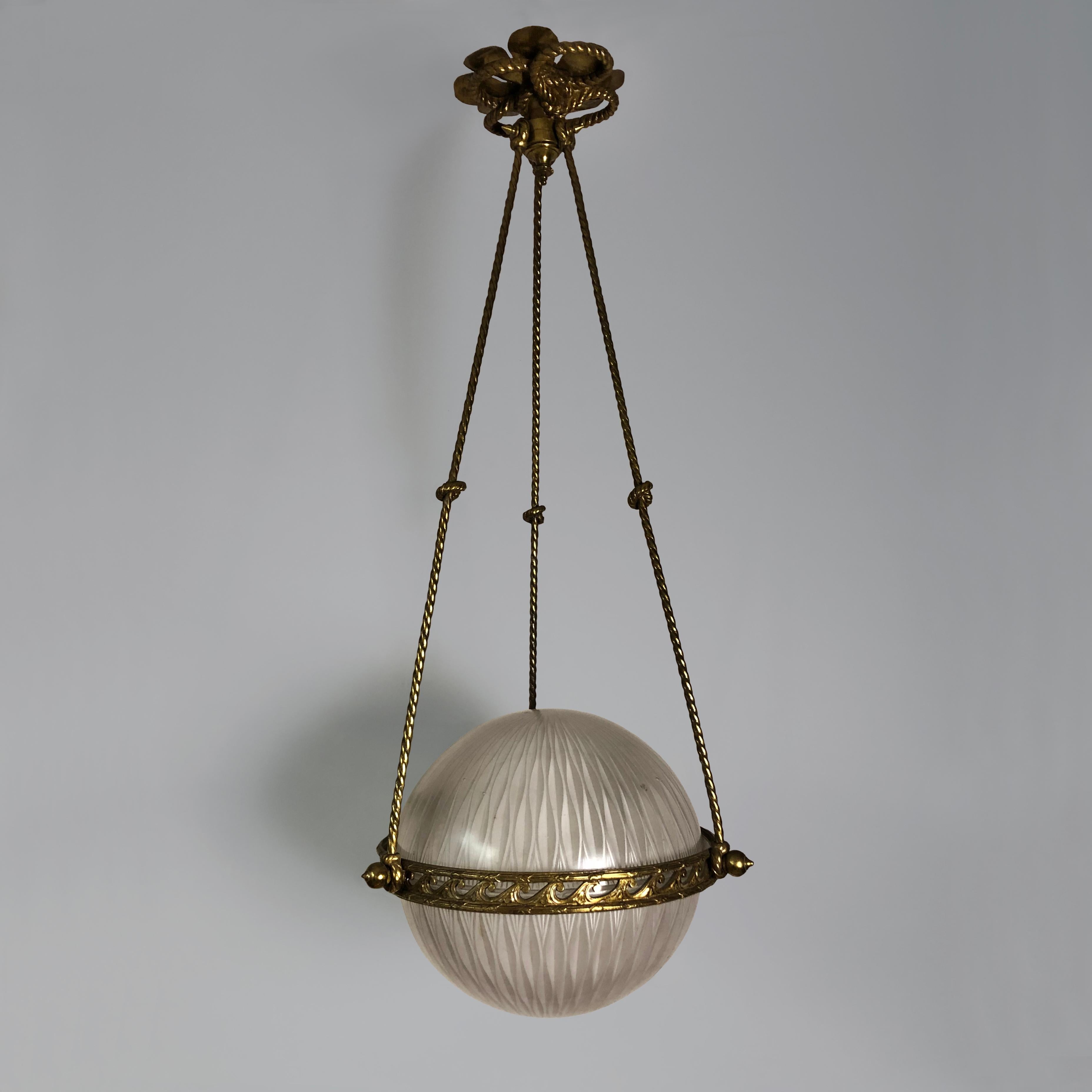 A very smart English 1920s globe pendant light suspended on three twisted brass rods in the form of ropes tied with knots. The central brass rim decorated with Vitruvian scrolls. The two-part glass shades are in perfect condition with a very subtle