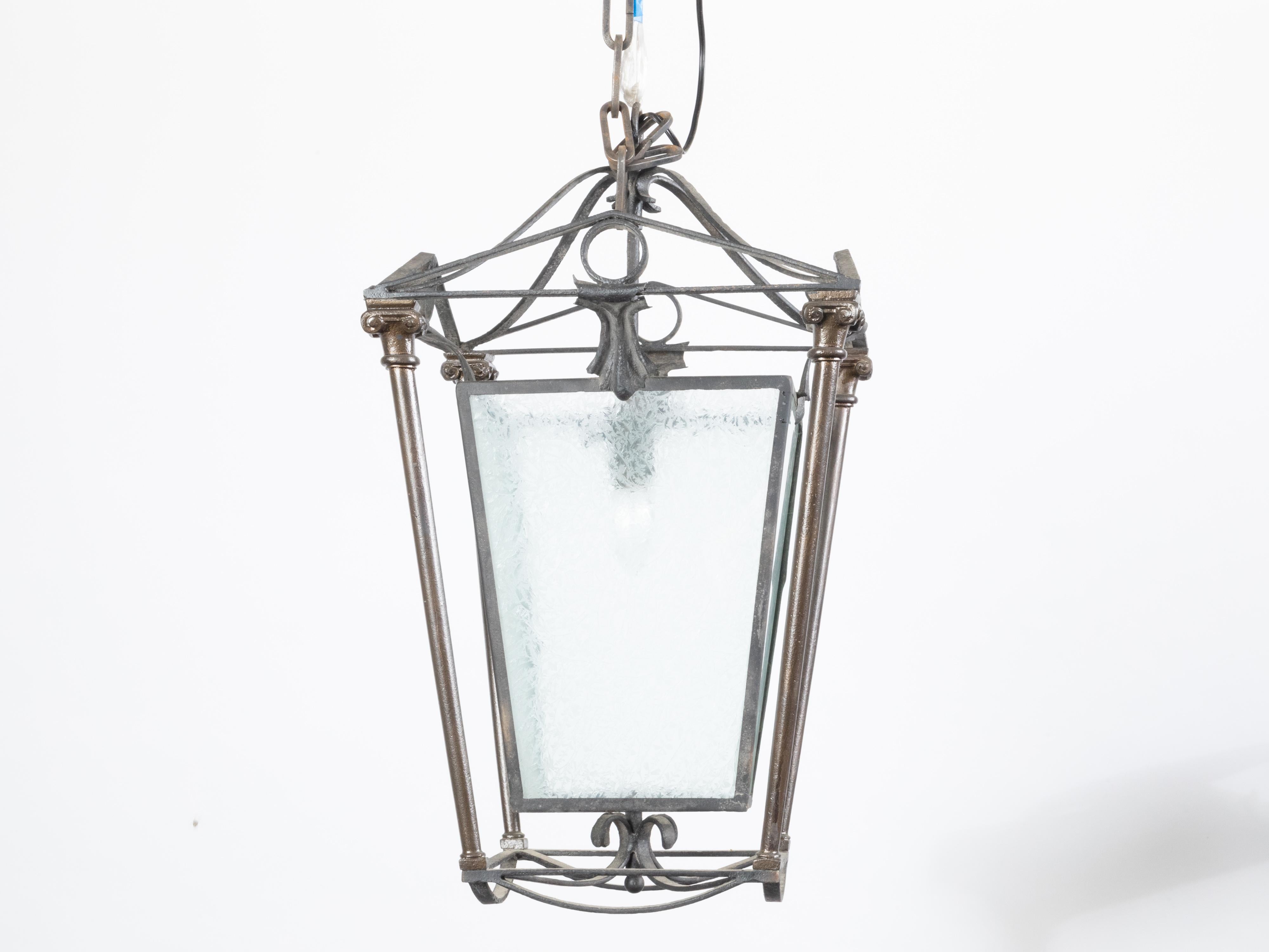 An English iron and brass lantern from the early 20th century, with single light and frosted glass panels. Created in England during the first quarter of the 20th century, this iron and brass lantern features four frosted glass panels securing a