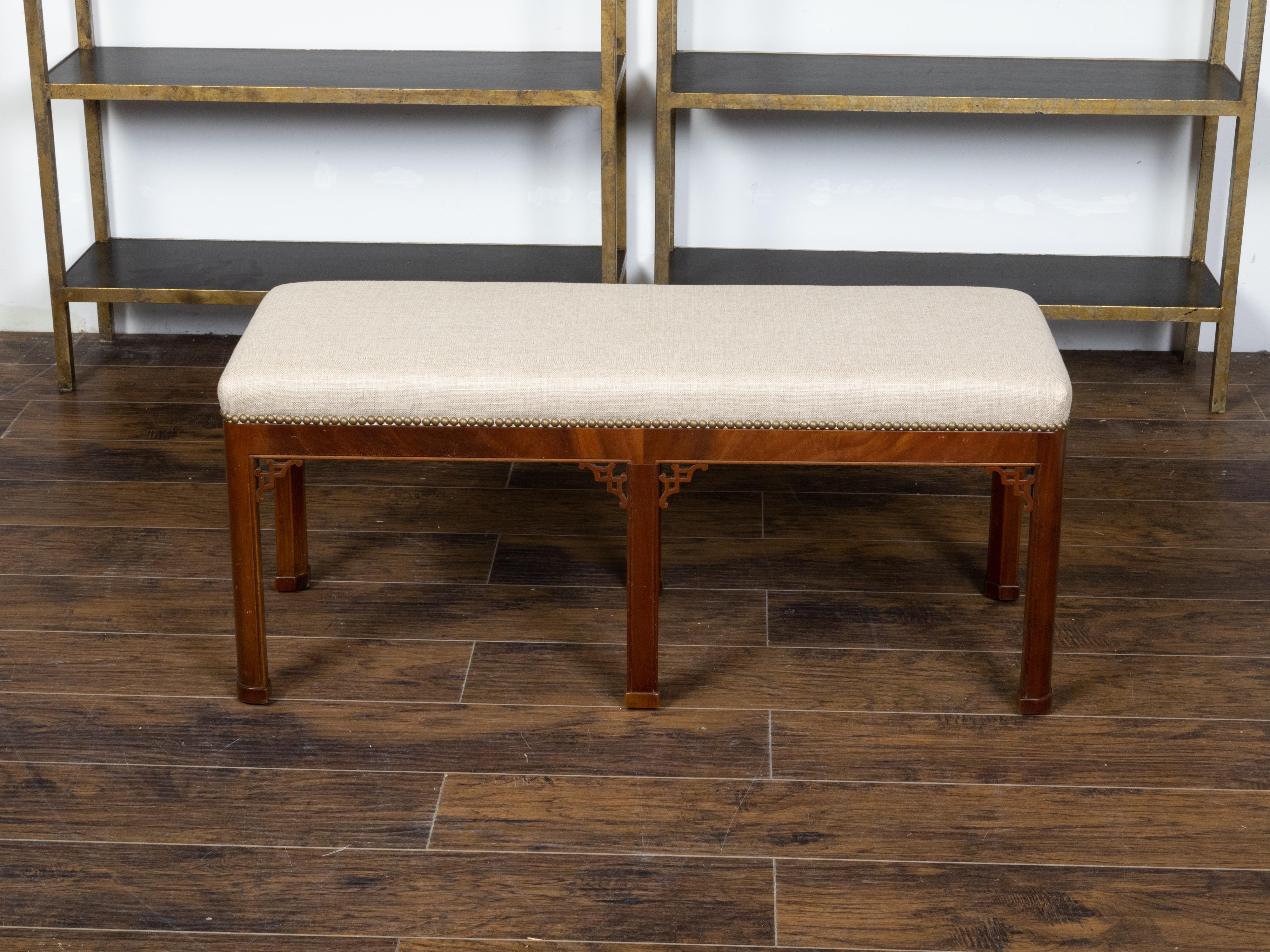 An English mahogany bench from the early 20th century, with fretwork motifs, straight legs and new linen upholstery. Created in England during the first quarter of the 20th century, this mahogany bench features a rectangular seat newly recovered