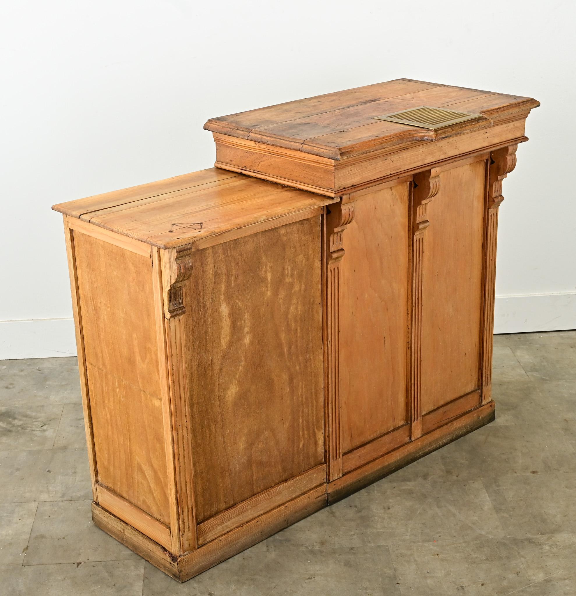 A small English pine bar from a pub from the 1920’s. This small serving bar is paneled on three sides with corbels and fluted columns and two surface levels. The top work surface has its original brass drip tray used to protect the wood from