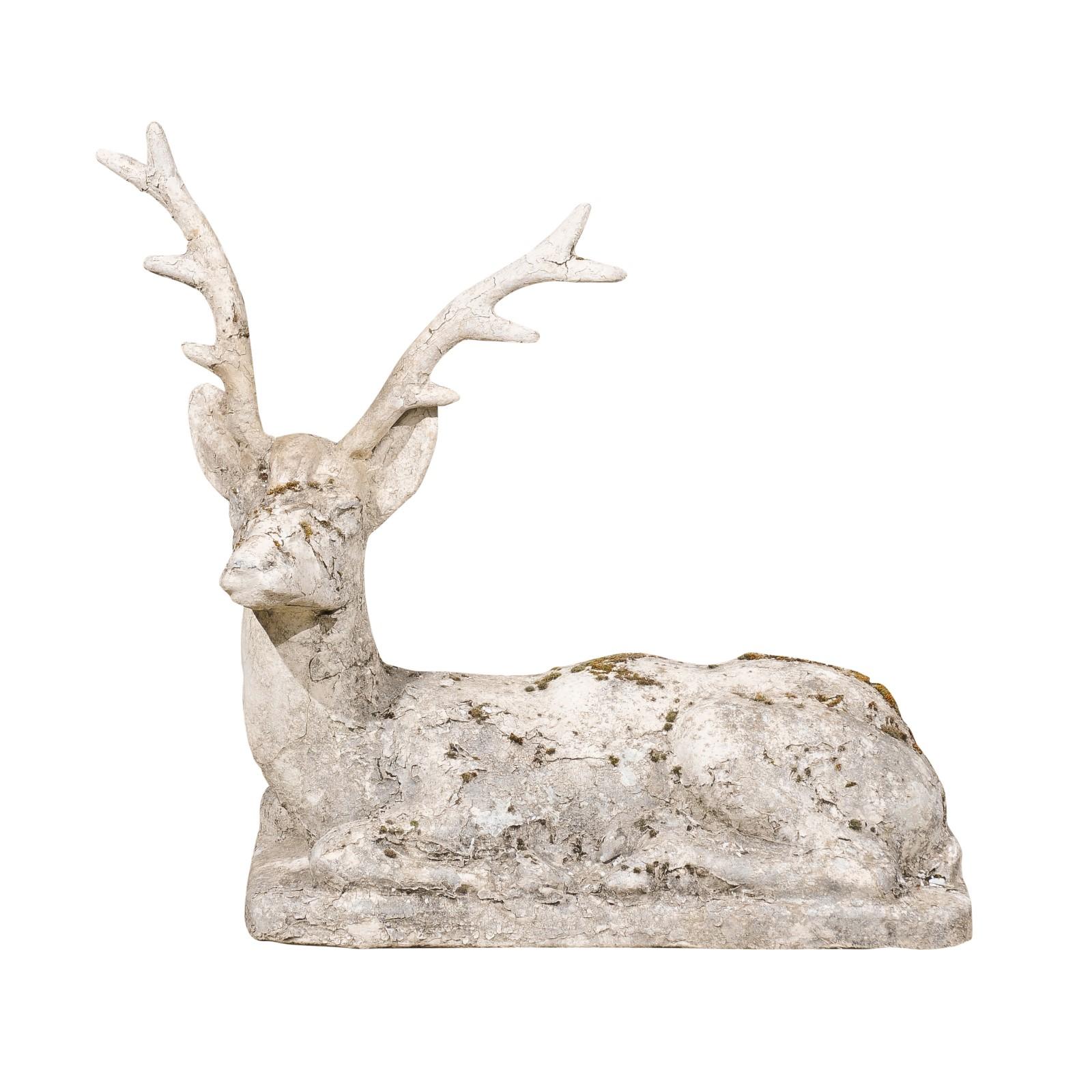 An English reconstituted stone reclining stag sculpture from the early 20th century, with nicely weathered patina. Created in England during the first quarter of the 20th century, this sculpture depicts a stag laying on a conforming base. Boasting a