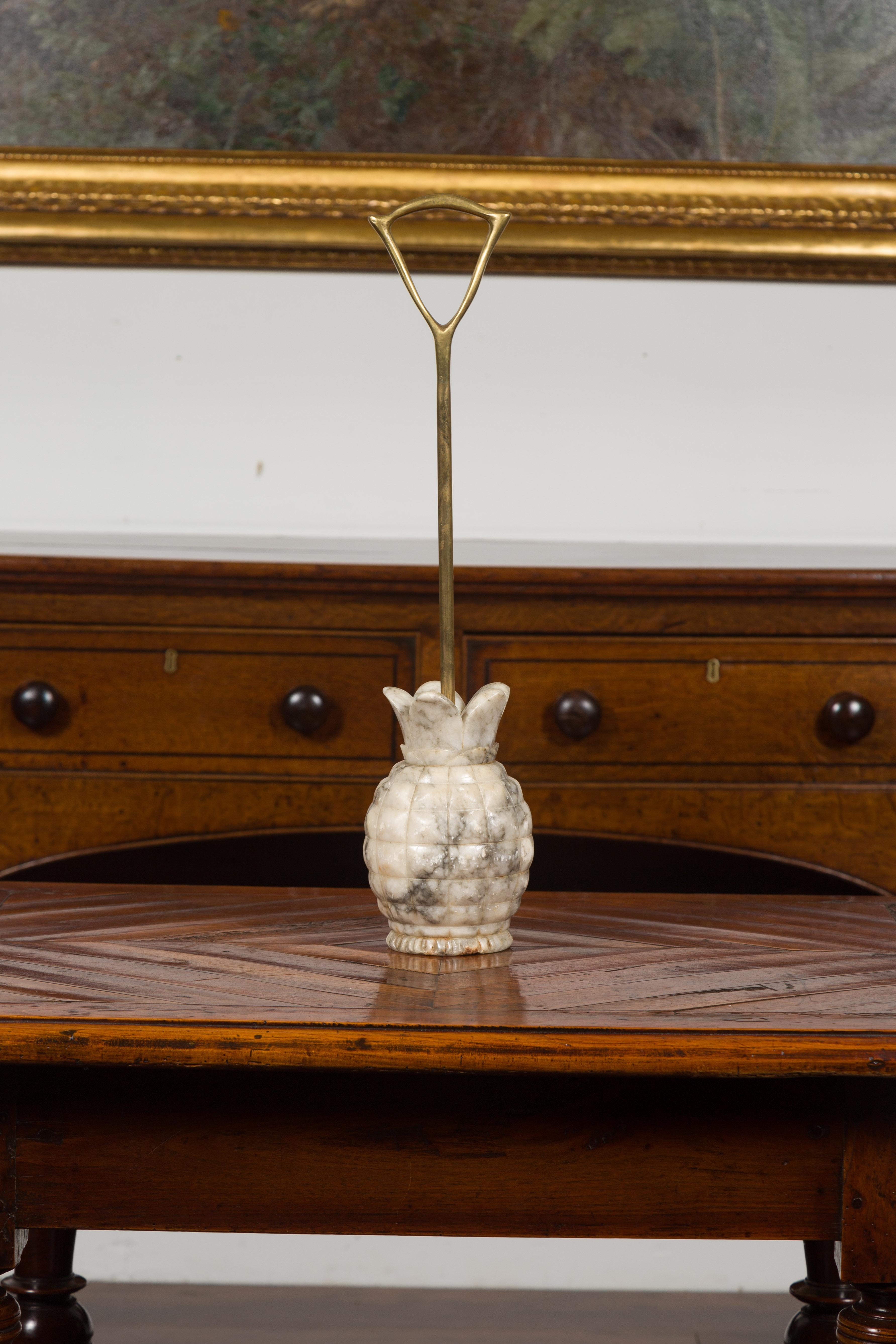 An English doorstop from the mid-20th century, with carved marble pineapple and brass handle. Created in England during the first half of the 20th century, this door porter features a marble pineapple base connected to a brass shaft and handle. A