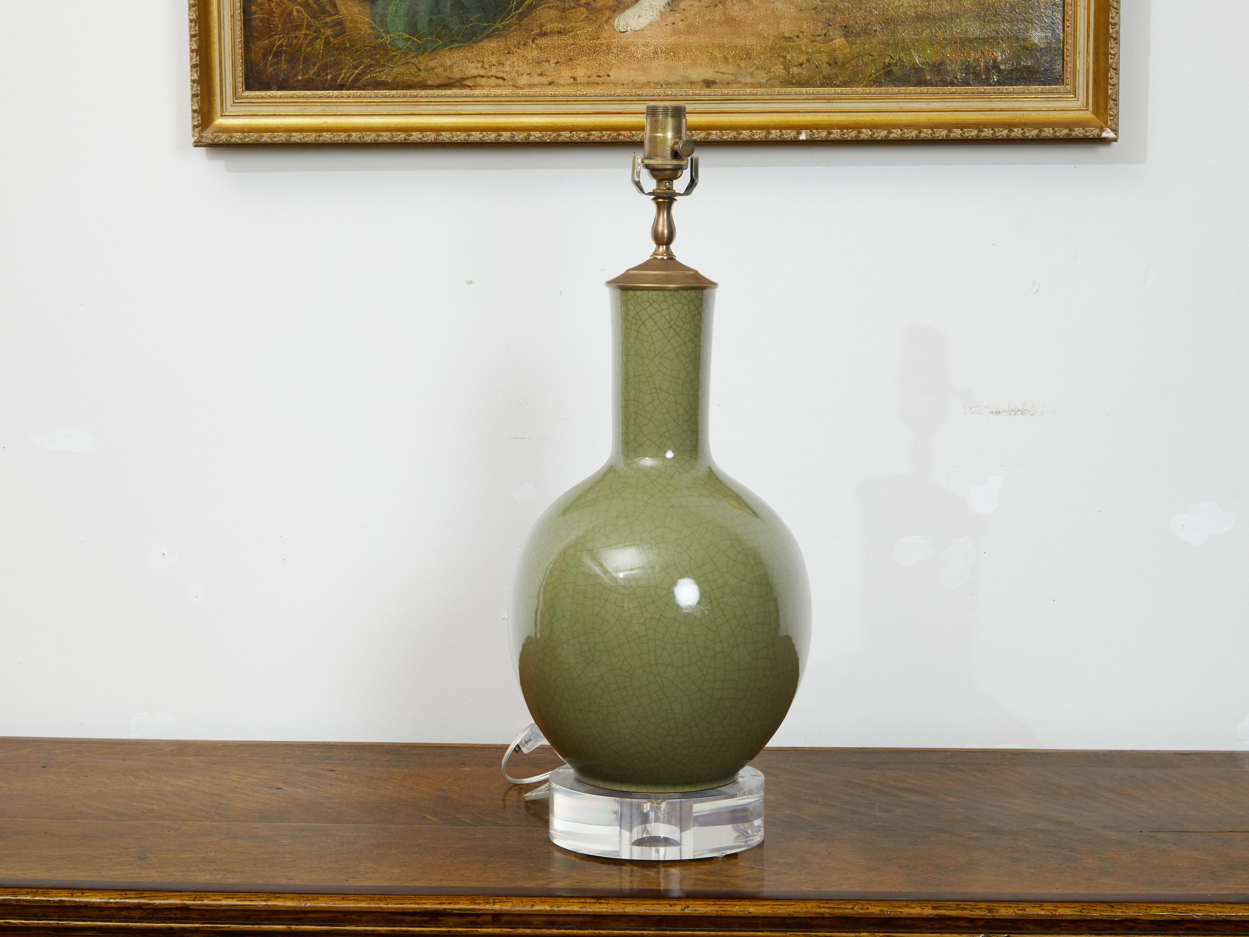 An English porcelain table lamp from the mid 20th century, with circular lucite base. Created in England during the second quarter of the 20th century, this porcelain lamp features a crackled green circular body with tall and narrow neck, mounted on