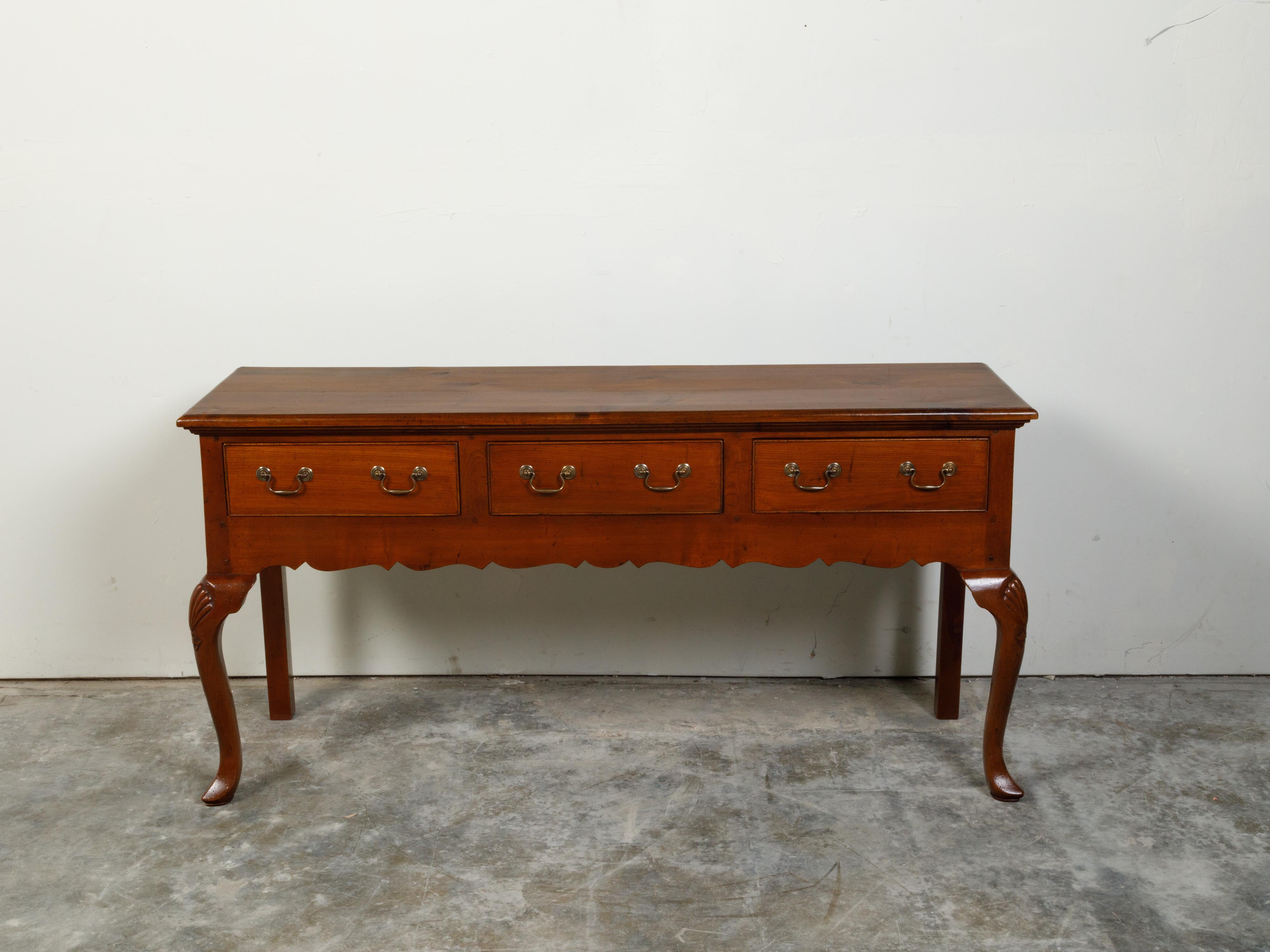 An English walnut or yew wood dresser base from the mid 20th century, with three drawers and carved apron. Created in England during the second quarter of the 20th century, this dresser base features a rectangular top sitting above three drawers