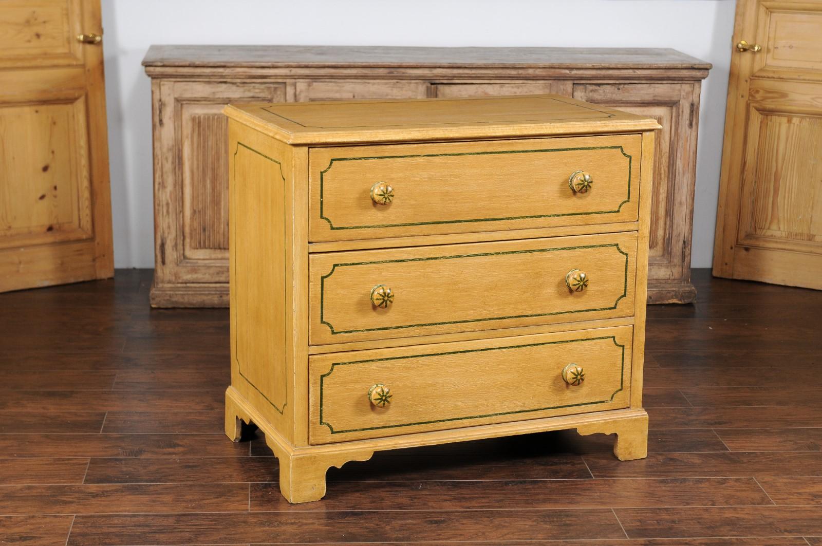 An English vintage painted three-drawer commode from the mid-20th century, with muted yellow finish and painted cartouches. This mid-20th-century English vintage commode, with its soothing muted yellow finish and delicately painted cartouches,
