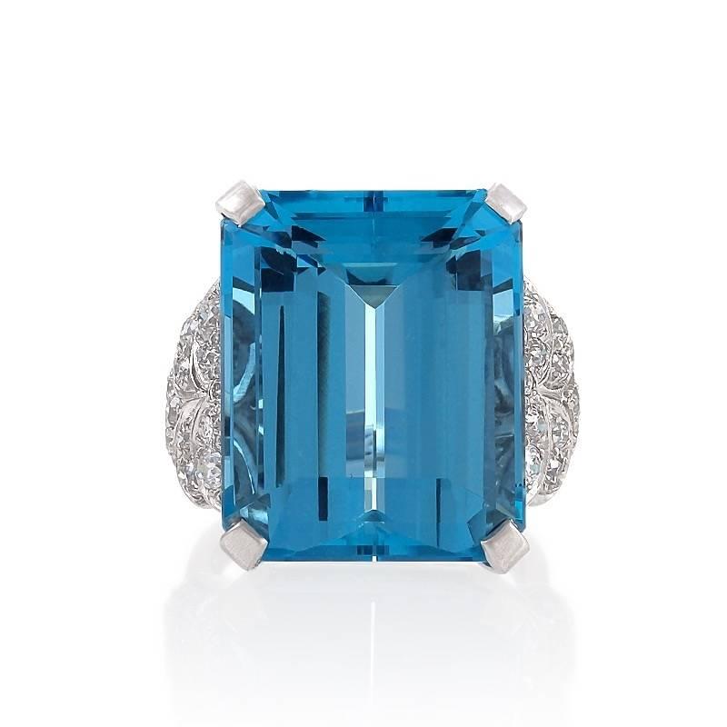 An English Mid-20th Century platinum ring with aquamarine and diamonds. The ring centers on an emerald-cut aquamarine with an approximate weight of 22.25 carats, set with 34 round-cut diamonds with an approximate total weight of .70 carat. The ring