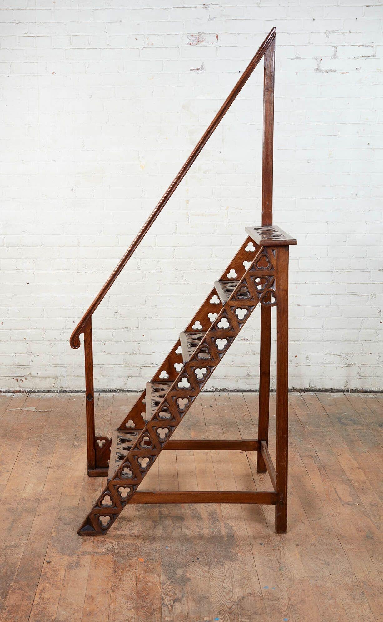 A set of English 19th century library steps with integral handrail.  In solid oak with decorative trefoil cutouts.  A useful piece that also lends an erudite and architectural element to any space.