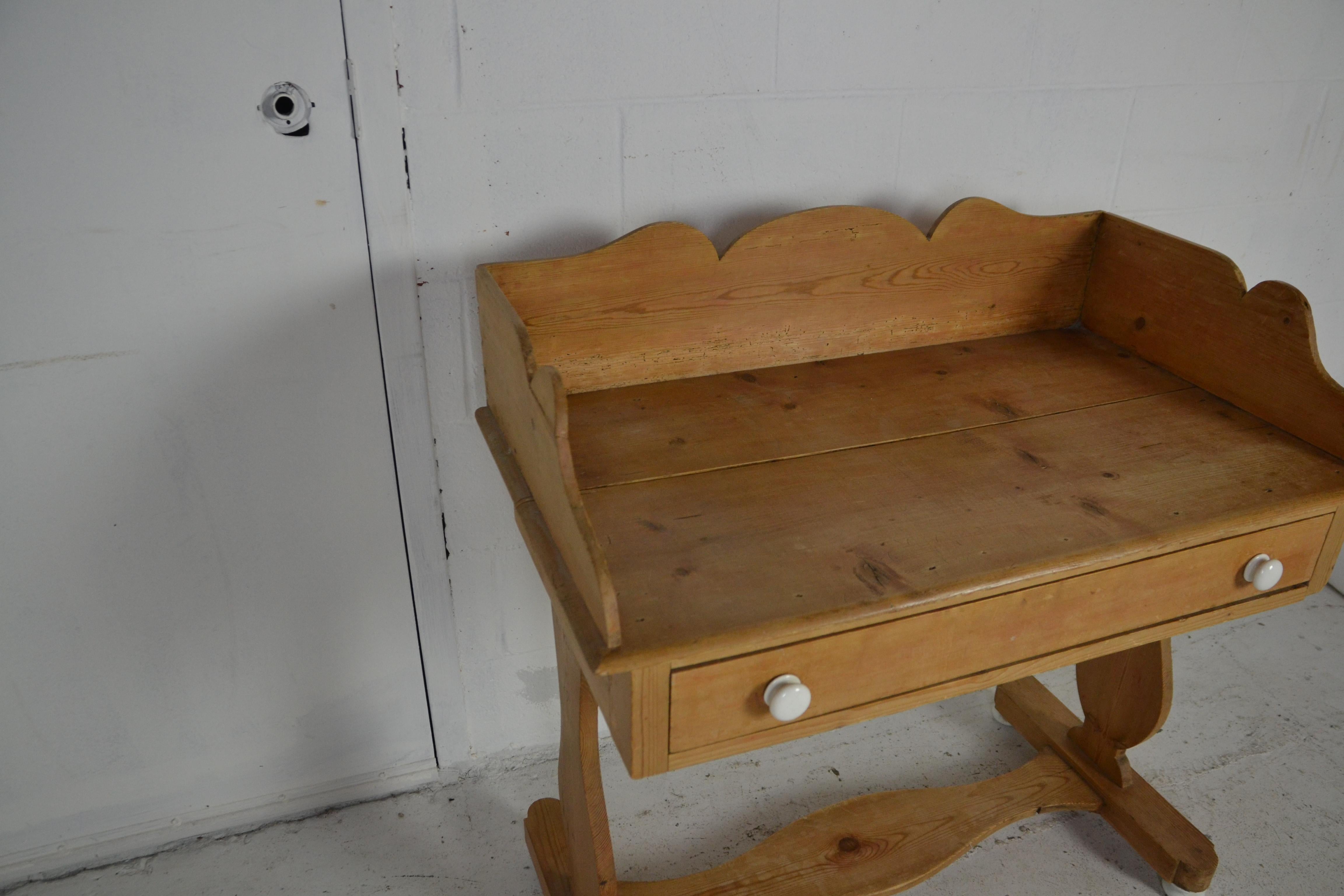 An English pine washstand with porcelain knobs and feet, circa 1870. Trestle base. One full length drawer.