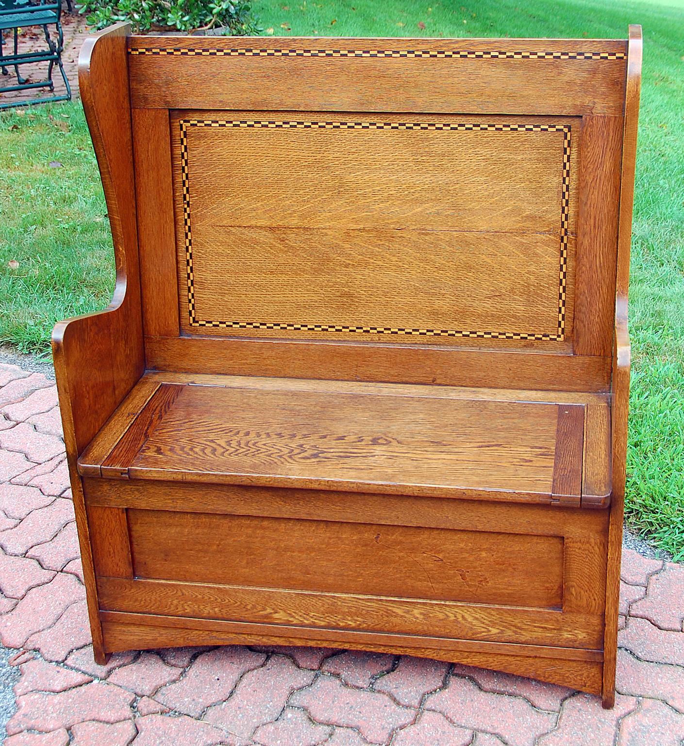 English 19th century Arts & Crafts settle, a high backed bench in oak with boxwood and ebony inlay by Shapland & Petter of Barnstable. This classic arts and crafts bench also has a seat which lifts to reveal considerable storage space, panel back