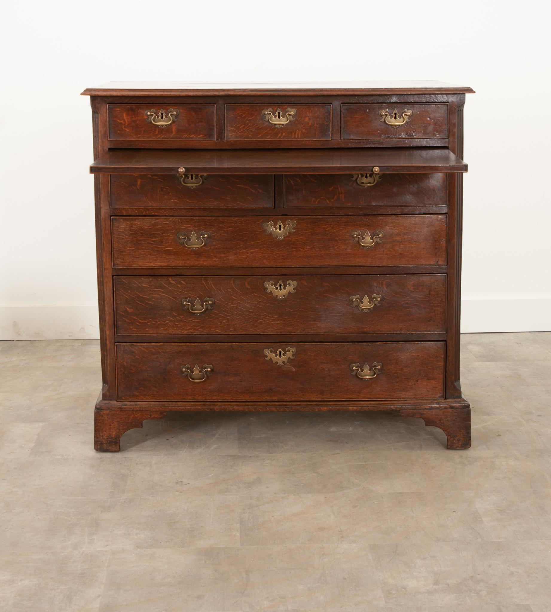 A classic, solid oak chest of drawers with a large pull-out linen folding slide over graduating drawers and bracket feet. Classic solid brass drawer pulls and escutcheon plates grace all the drawer fronts. No keys are present, however the pulls make