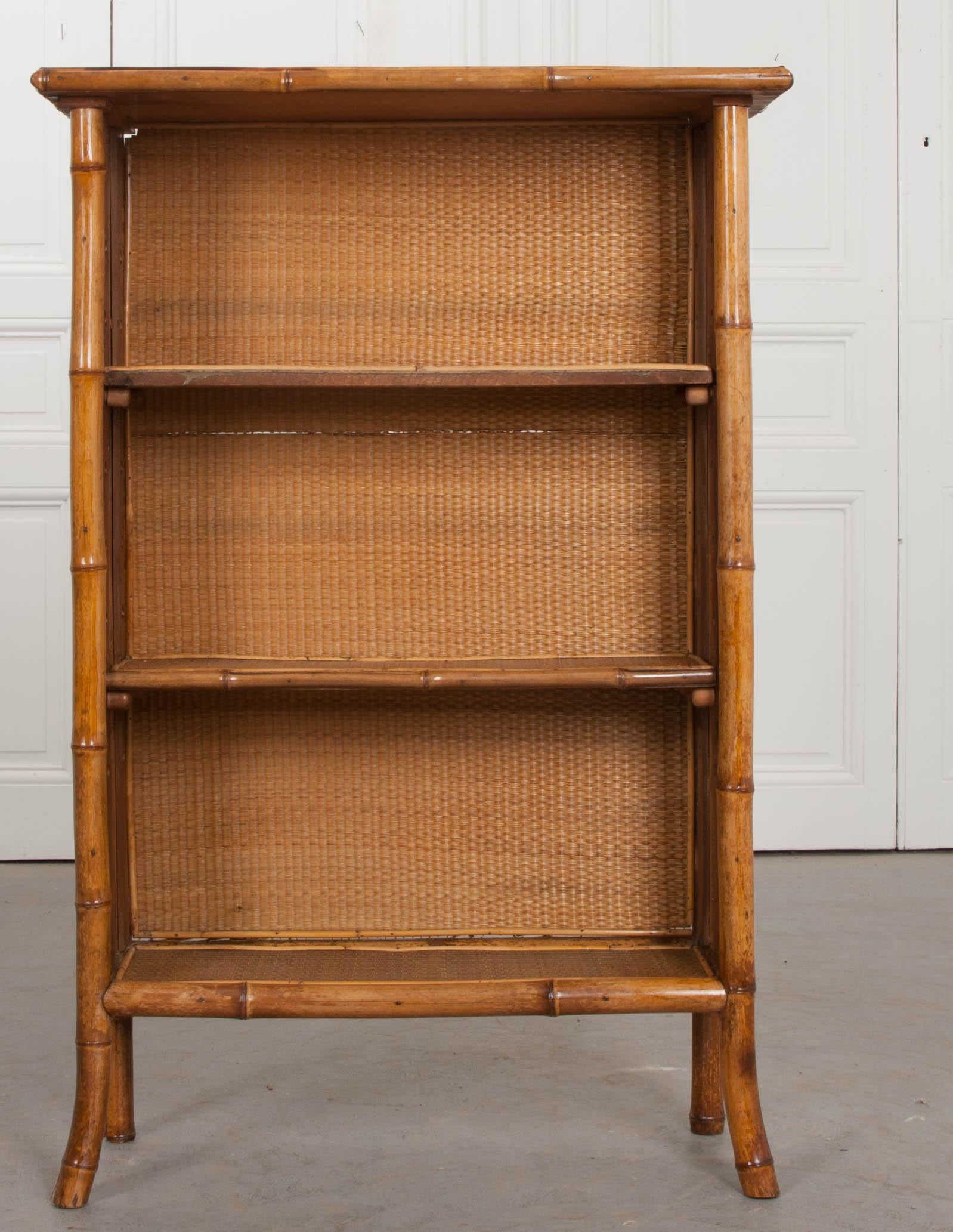 A wonderful English bamboo bookshelf from the 1890s, that has been recently refinished. It has been finished in a gorgeous black and gold découpage. The woven seagrass found in the interior is remarkably intact. This small bookcase has two centre