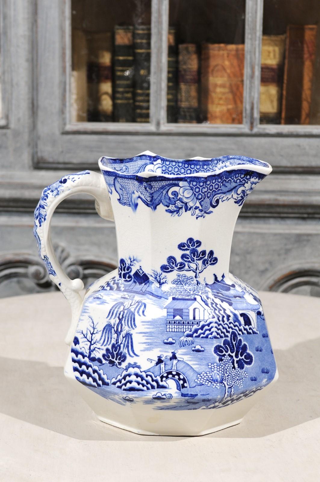 An English blue and white Mason's patent ironstone pitcher from the 19th century, with chinoiserie décor depicting two fishermen on a bridge and willow patterns. Born in England during the 19th century, this exquisite pitcher features an octagonal