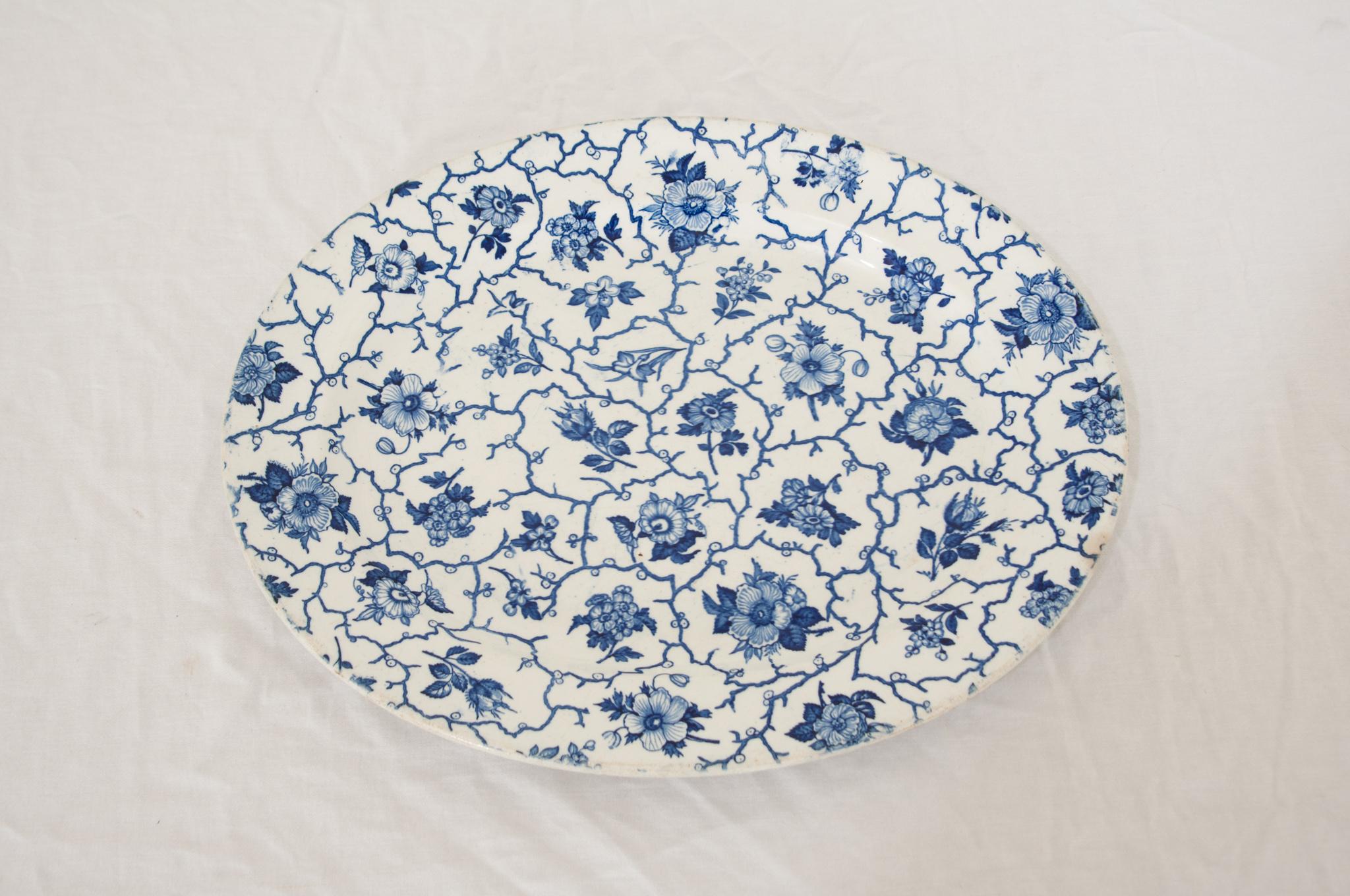 An English 19th Century antique ceramic serving platter. This lovely large transferware platter is decorated in a pretty and alternating mix of blue florals with a stylized dynamic running spray of budding vines across the entire piece. Nice and