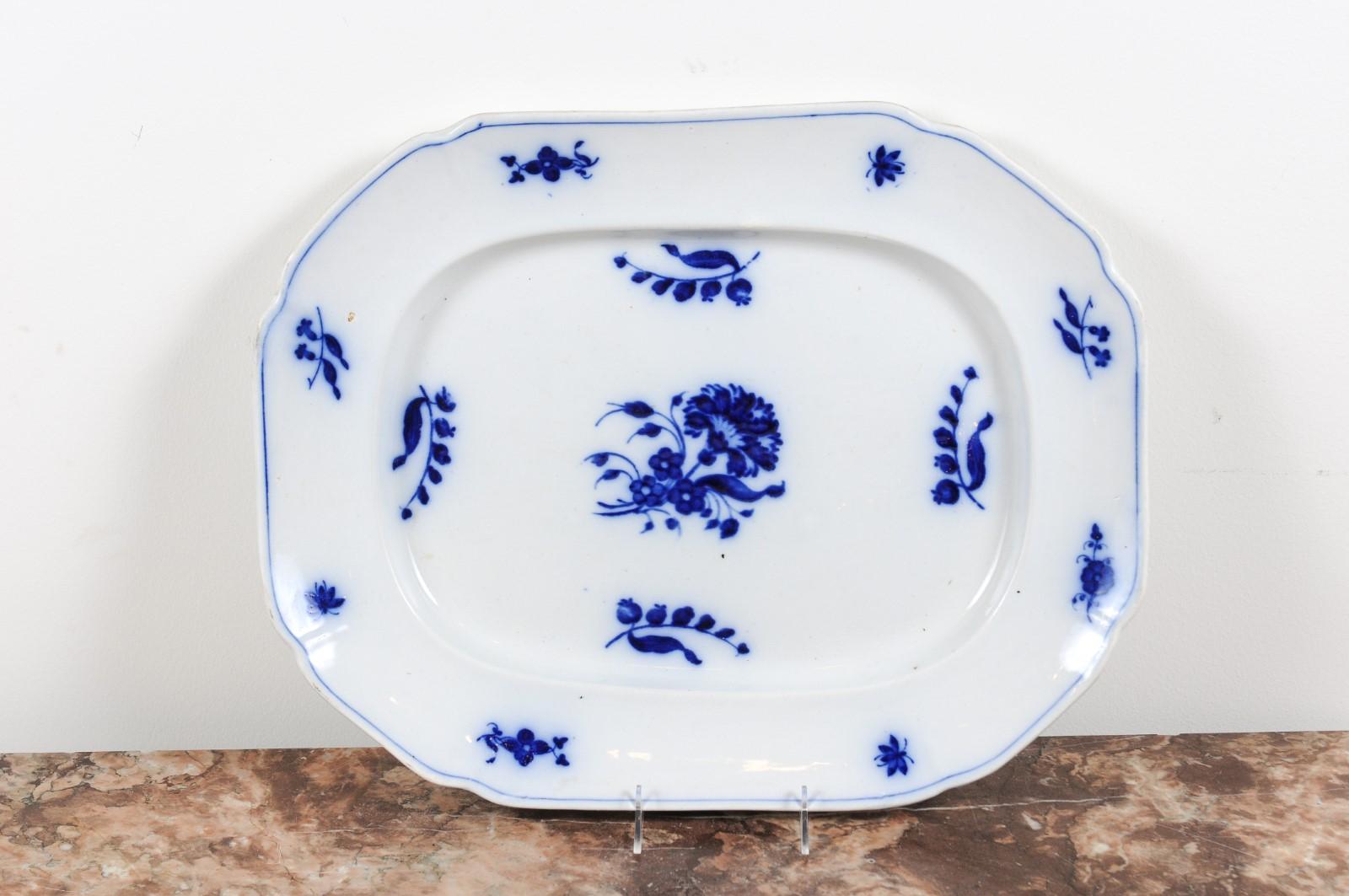 An English blue and white platter from the 19th century, with floral decor. Born in England during the 19th century, this platter features blue floral motifs standing out on a white ground. Presenting a slightly scalloped edge highlighted by a thin