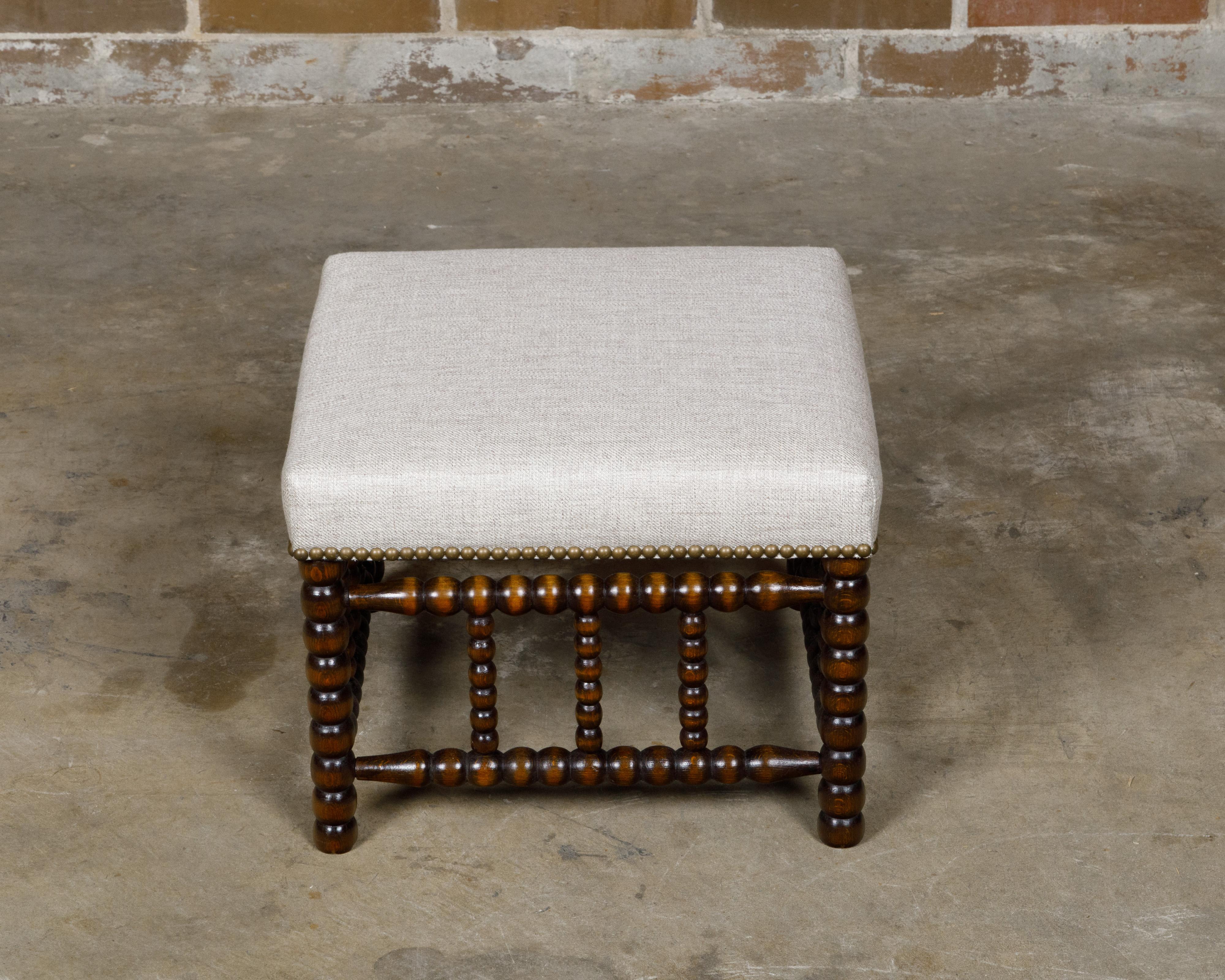 Tabouret anglais du 19e siècle avec siège tapissé de lin et garniture en tête de clou en laiton. Apportant un charme intemporel à n'importe quel espace, ce tabouret bobine anglais du 19ème siècle capte notre attention avec son artisanat exquis et