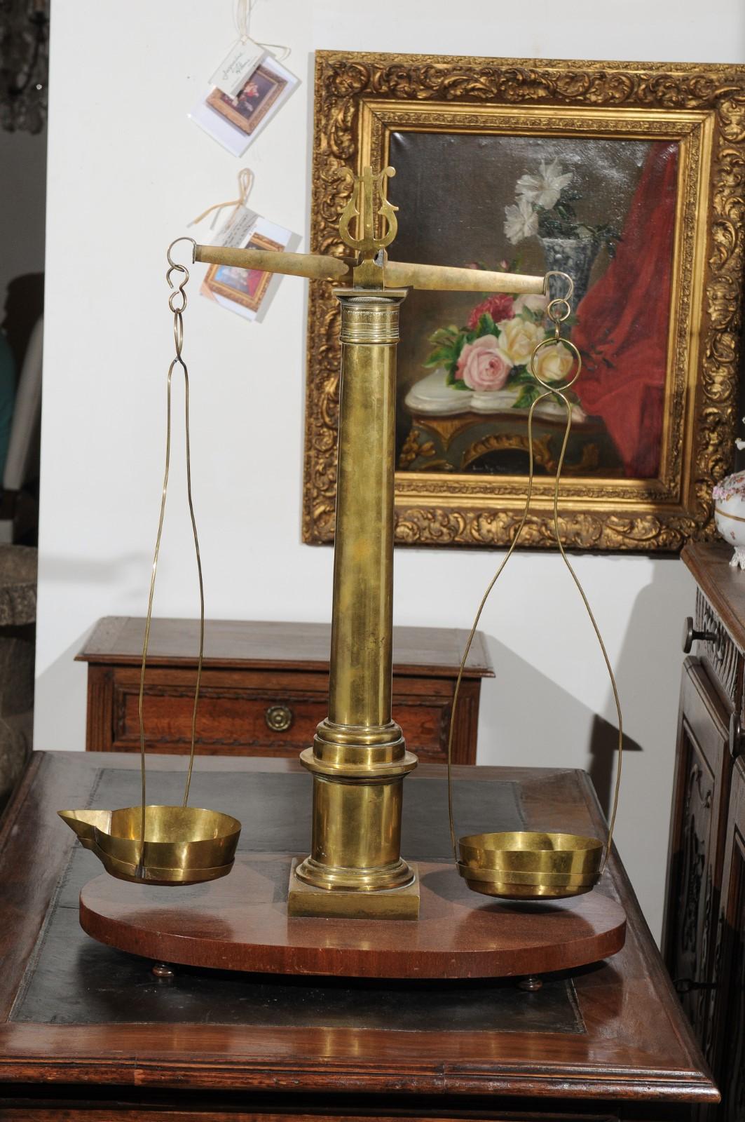 An English brass herbalist scale from the 19th century, with column and lyre details, mounted on a wooden base. Used to measure herbs, this exquisite scale features a brass structure presenting a central column adorned with a capital topped with a