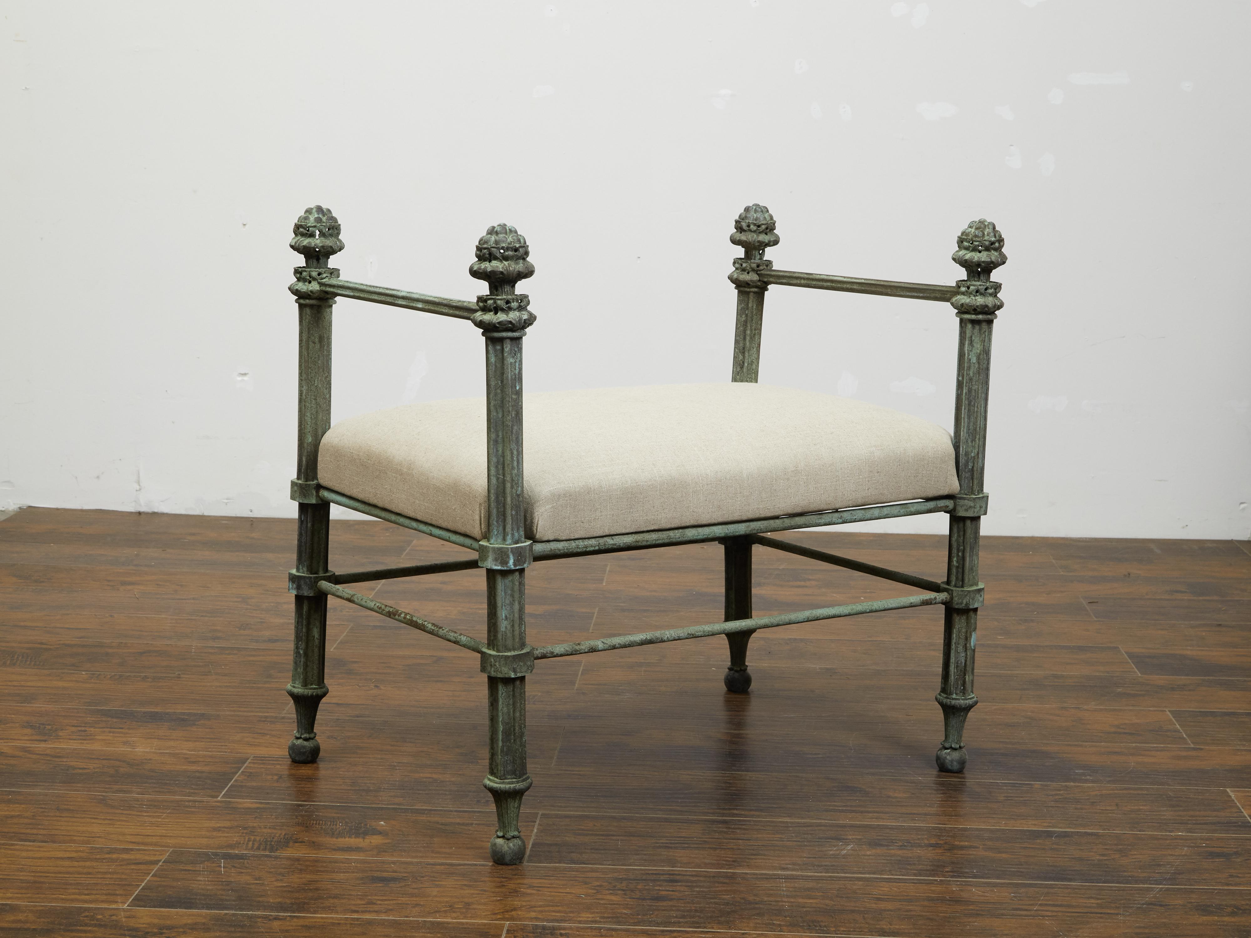 An English bronze bench from the 19th century, with fluted supports, finials and new upholstery. Created in England during the 19th century, this bronze bench features a rectangular seat newly recovered with a neutral toned fabric highlighting the